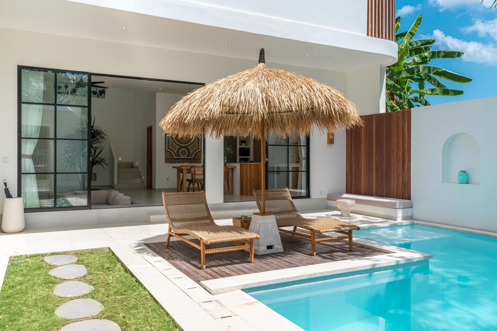 Timber loungers on the deck built out into the water beneath an alang-alang parasol