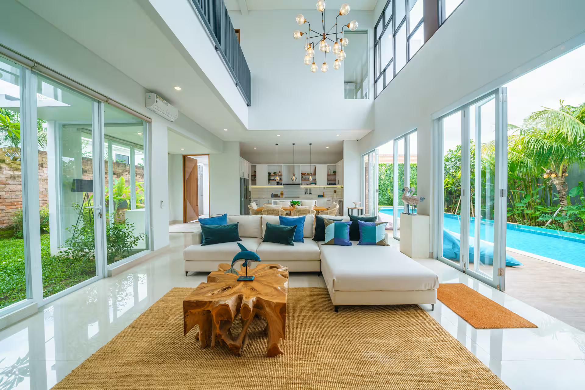 Double-height living room opening through glass to the pool, jute rug and teal cushions