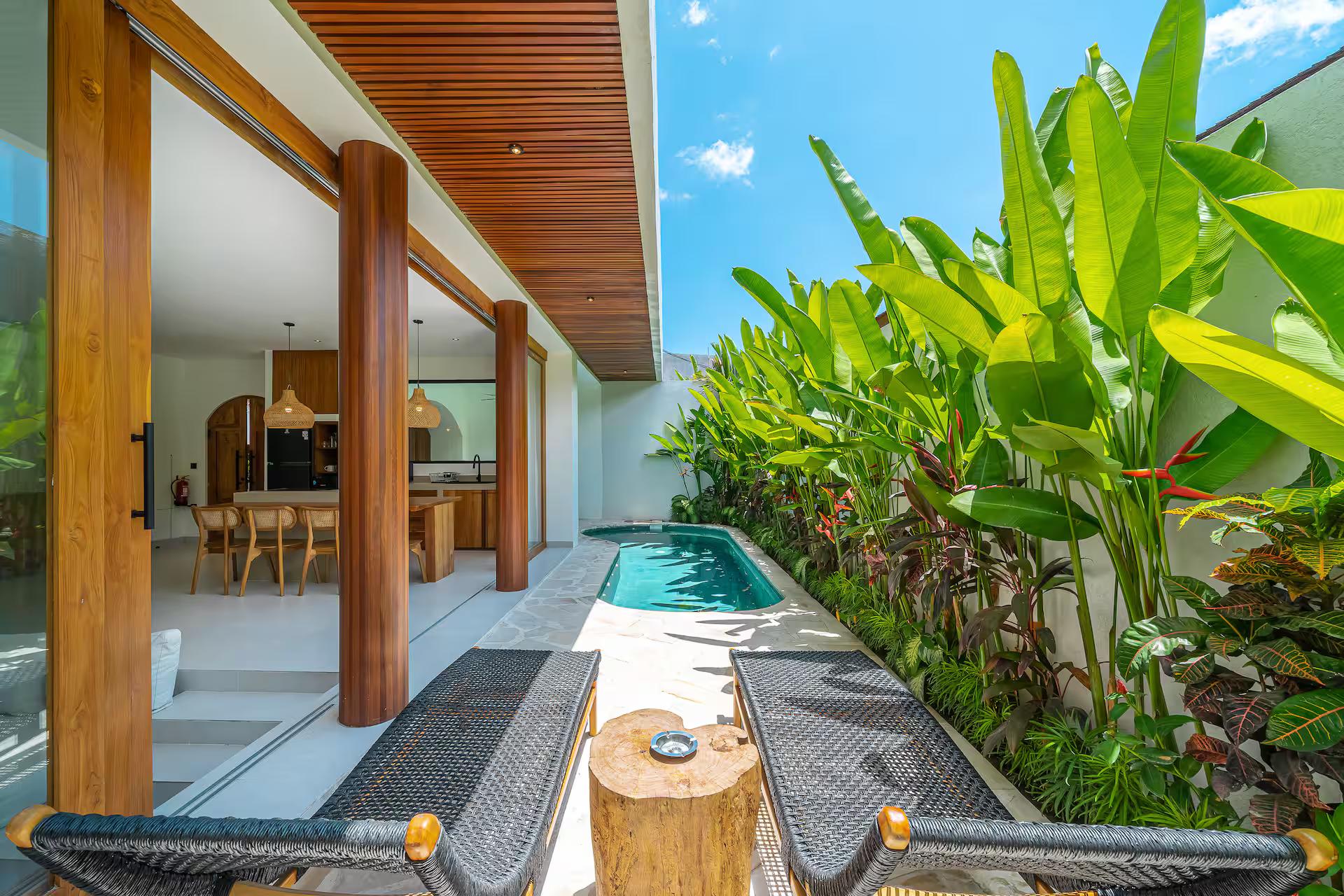 Sun loungers and a sawn-log side table beside the pool, banana leaves overhead