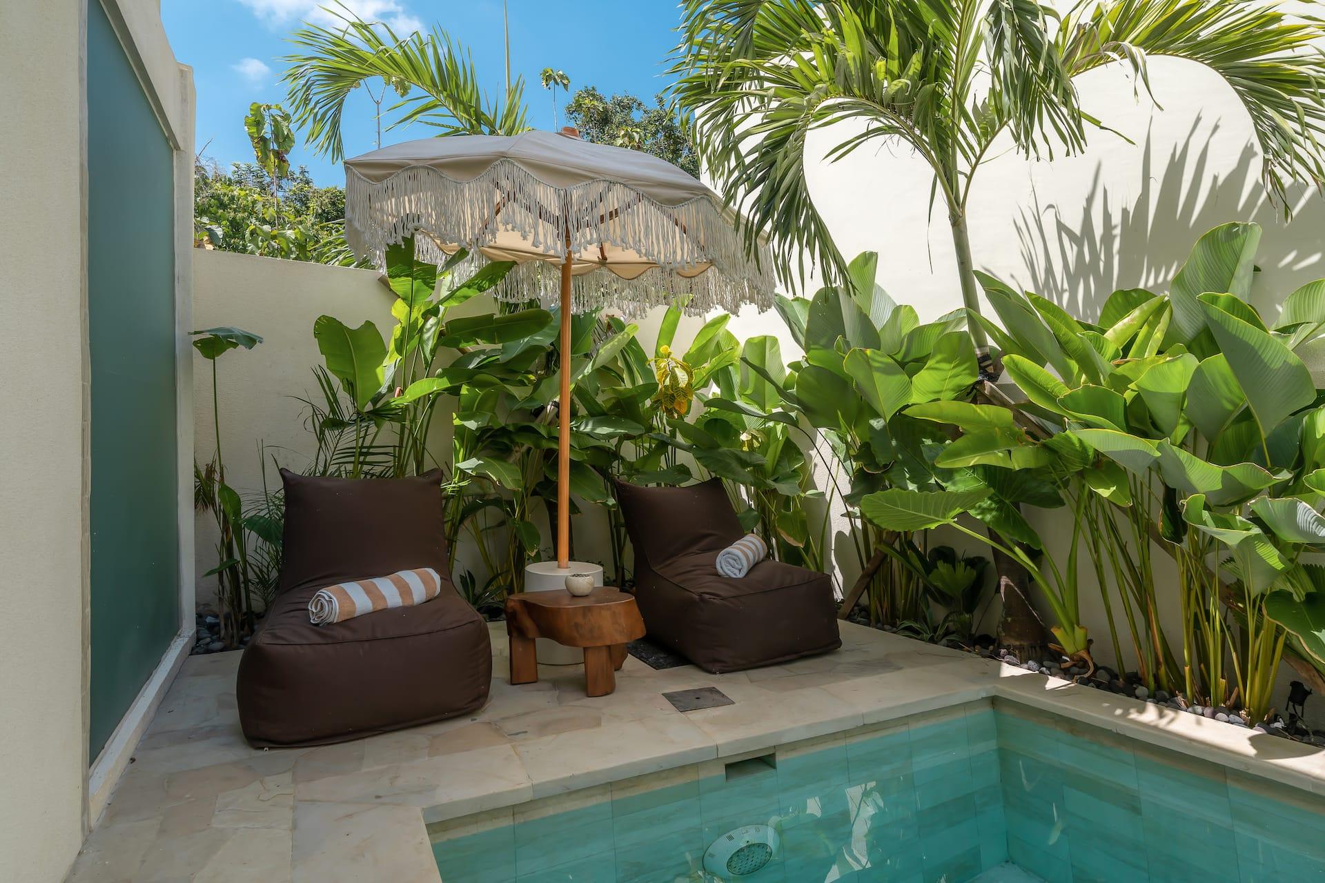 Two beanbags and a fringed Balinese umbrella set on the travertine terrace beside the pool