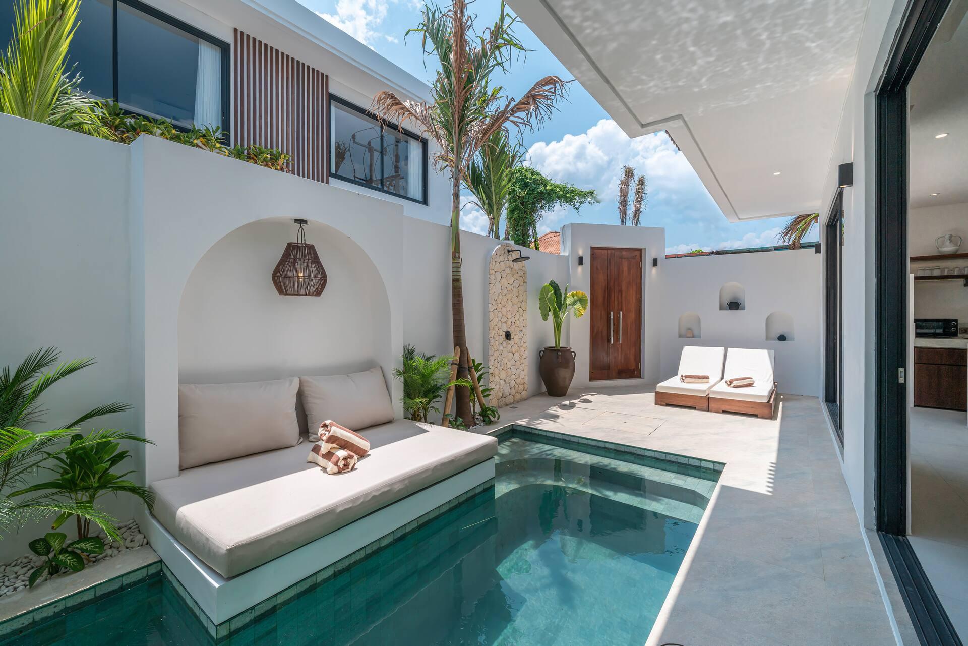Cushioned daybed set into an arched alcove at the pool edge, with a sun bed opposite