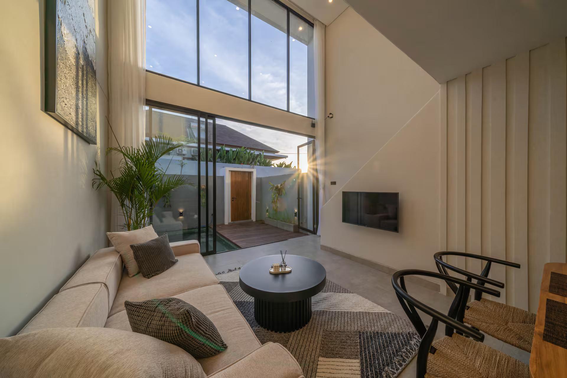 Double-height living room with a cream sectional and black drum table, glazed to the courtyard