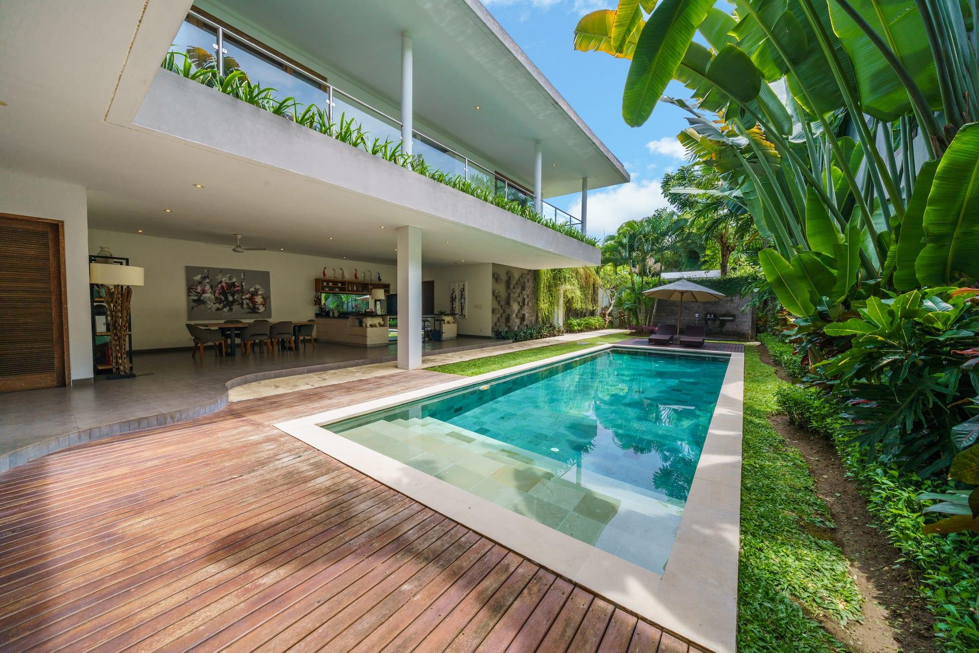 Timber sun deck running alongside the lap pool, banana palms crowding the boundary wall