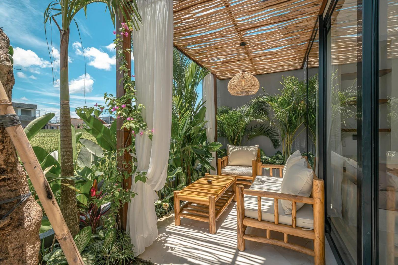 Teak sofa and armchairs under the bamboo pergola, gauze curtains drawn back