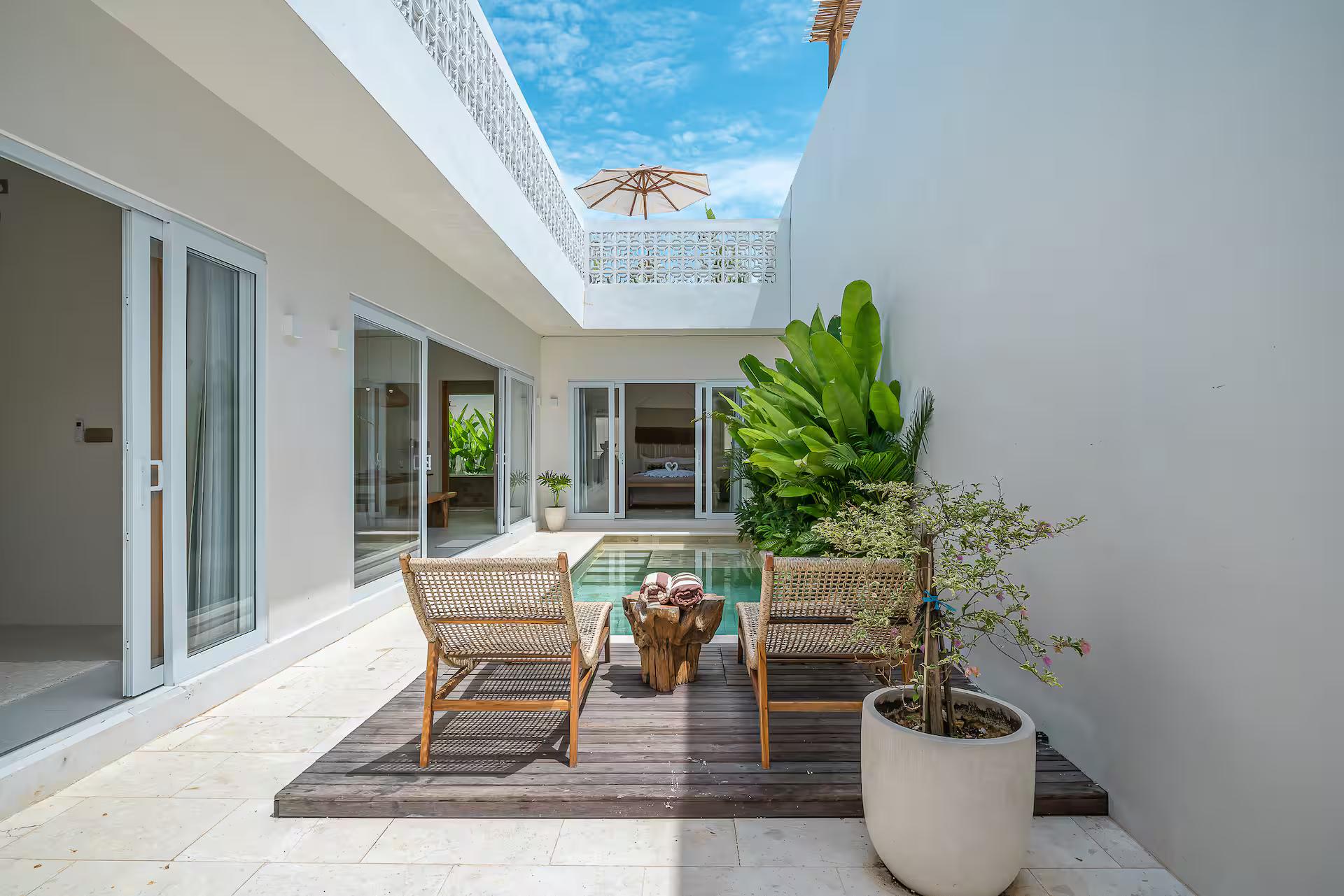 Timber deck at the end of the pool with two chairs and a potted plant, open sky above