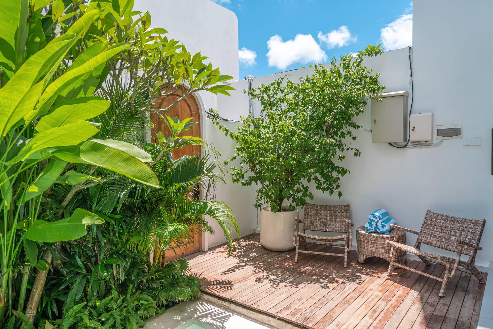 Timber deck with woven lounge chairs and a potted tree beside the pool garden at Villa Dharma
