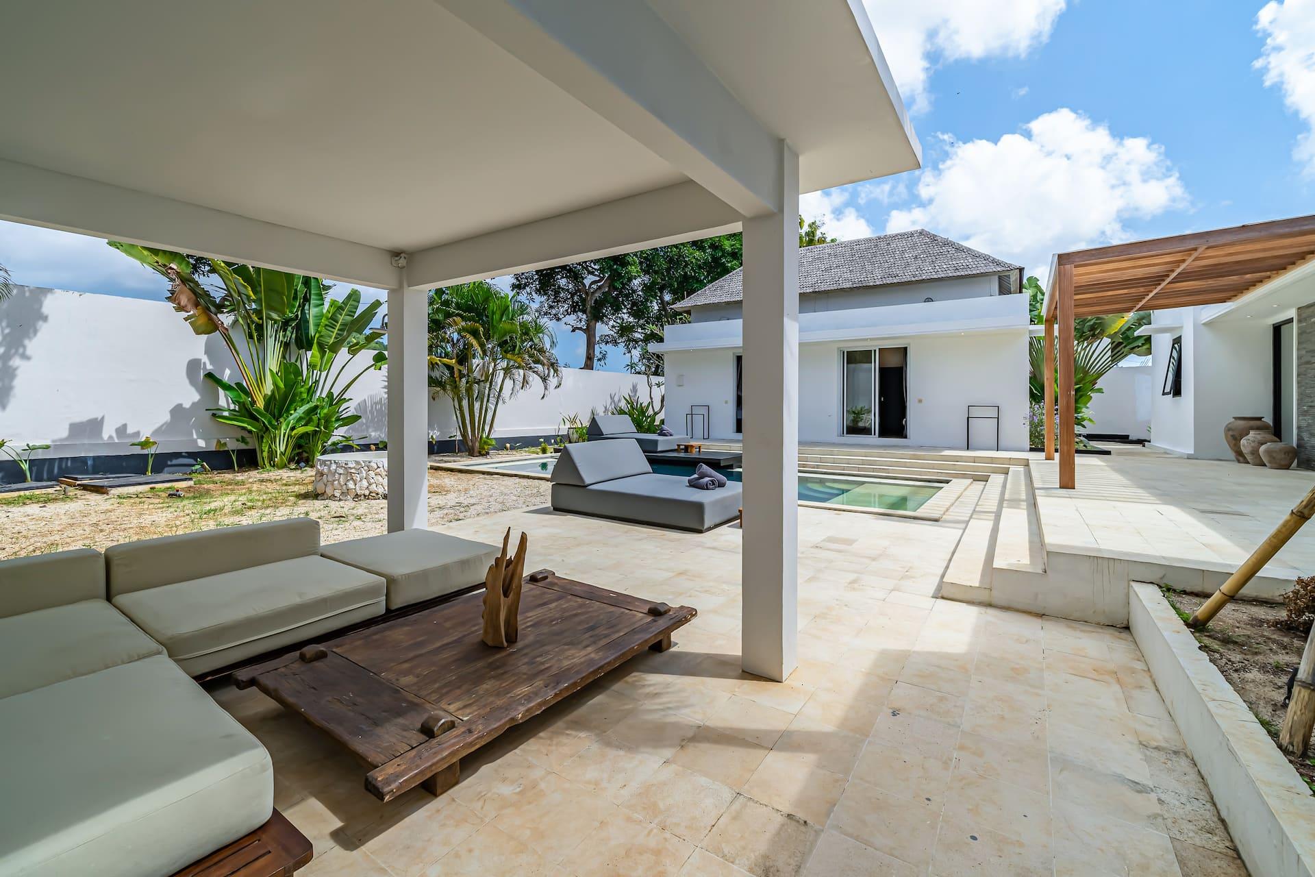 Shaded lounge pavilion with cream sofas and a rustic timber coffee table beside the pool
