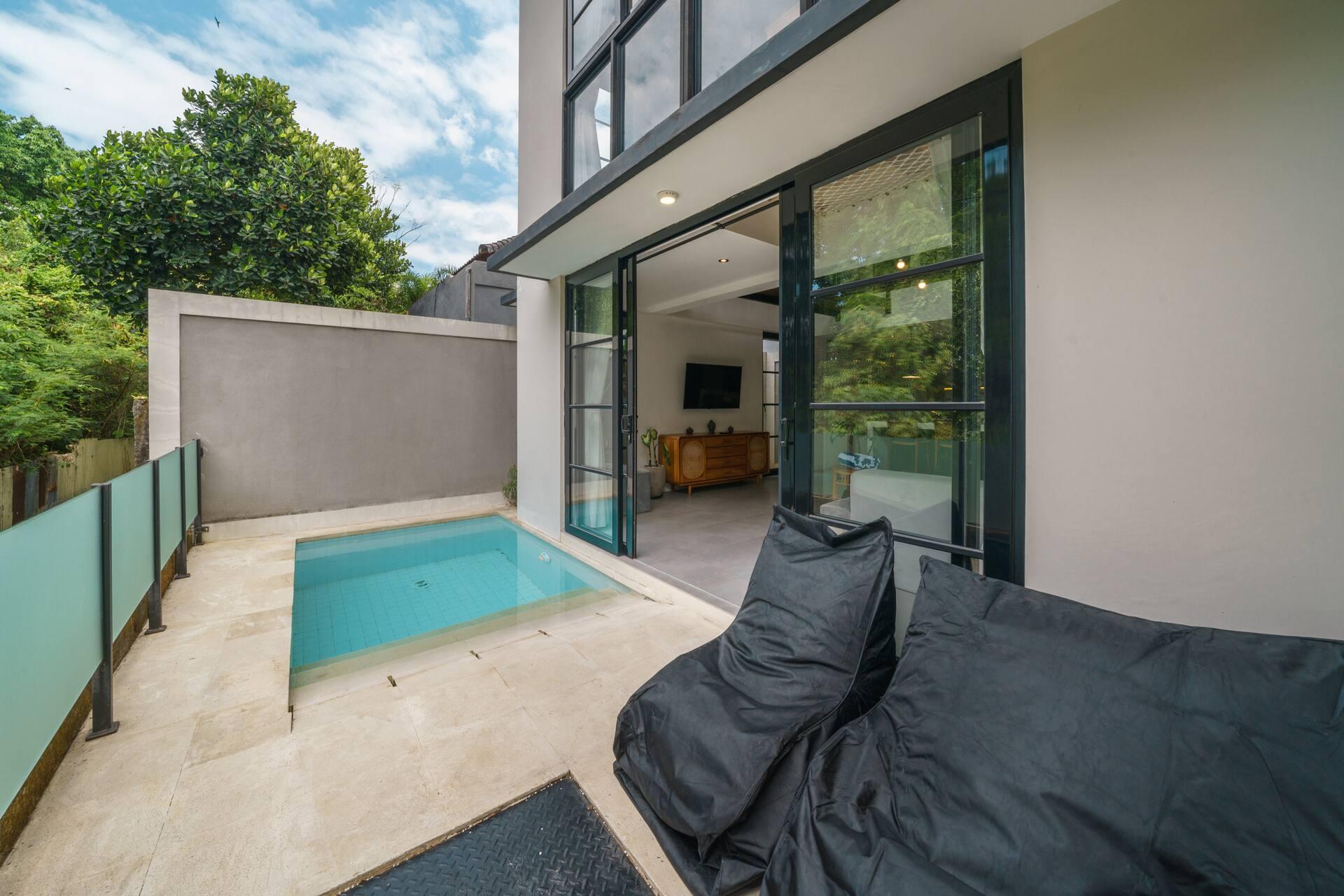 Poolside deck with black beanbags beside steel-framed glass doors that open into the living room