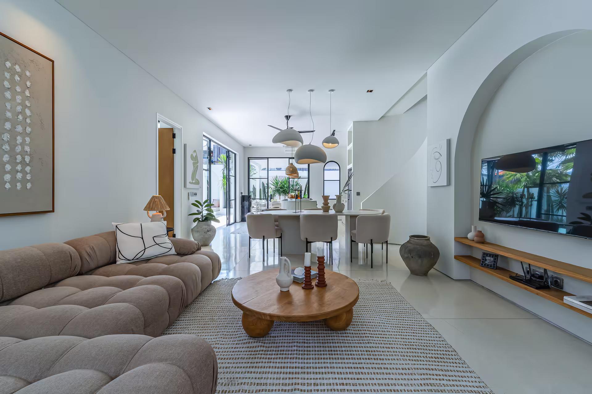 Living room at Sanctum House with a deep tufted sectional, round timber table and kitchen beyond
