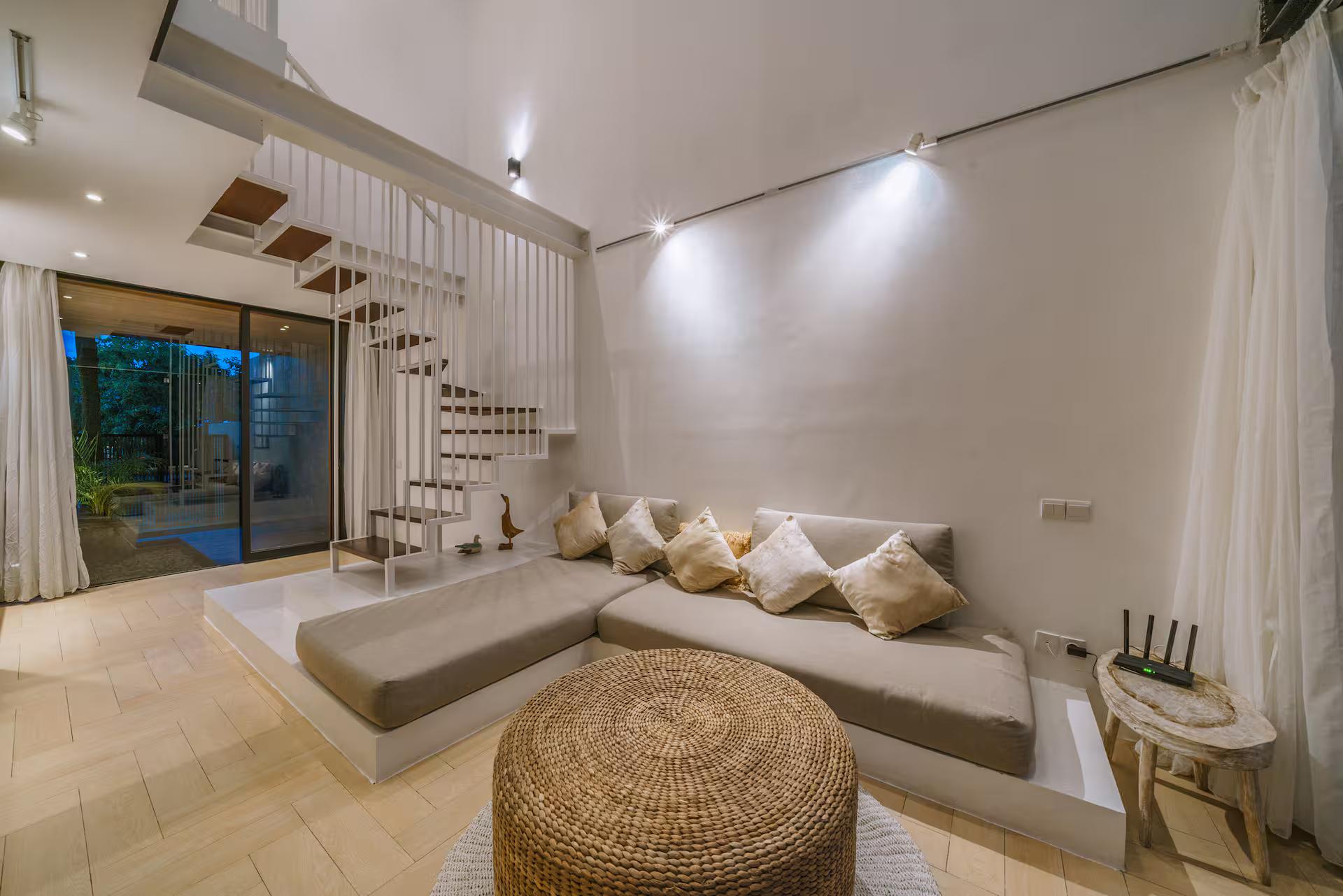 Double-height living room at Villa RIZR with a long plaster banquette and a woven pouffe