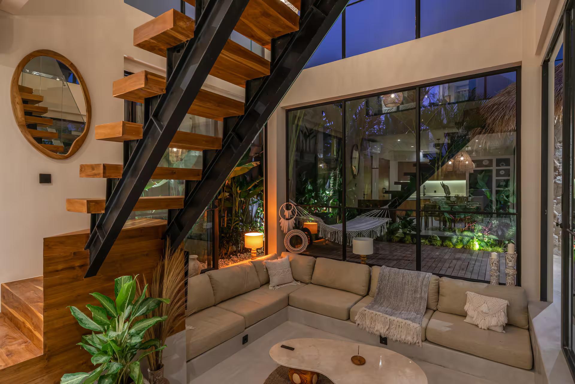 Sunken living room with a teak open-tread staircase rising through a double-height glass wall