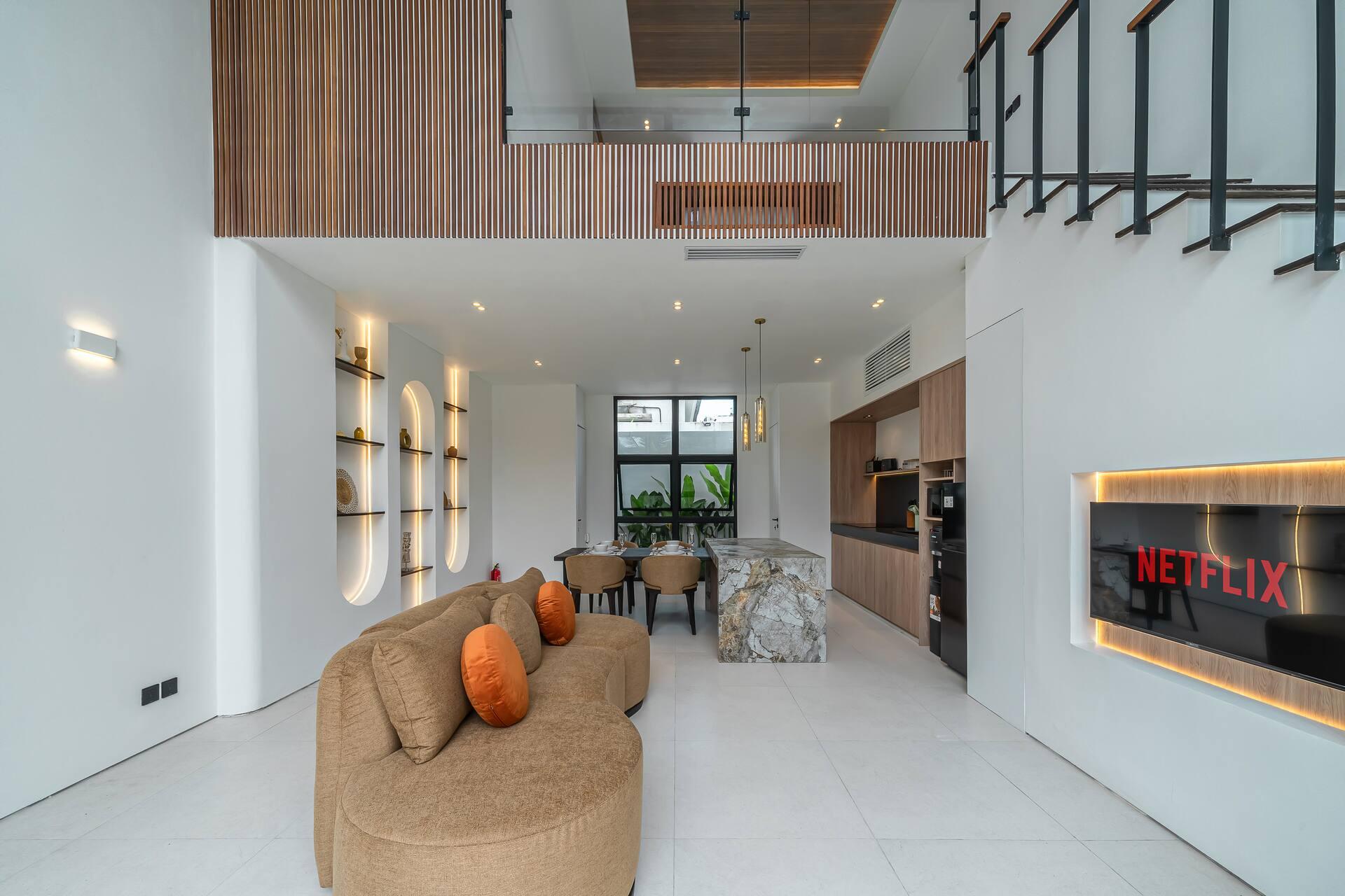 Double-height living room at Fire Villa Berawa with curved sofa, marble island and floating staircase