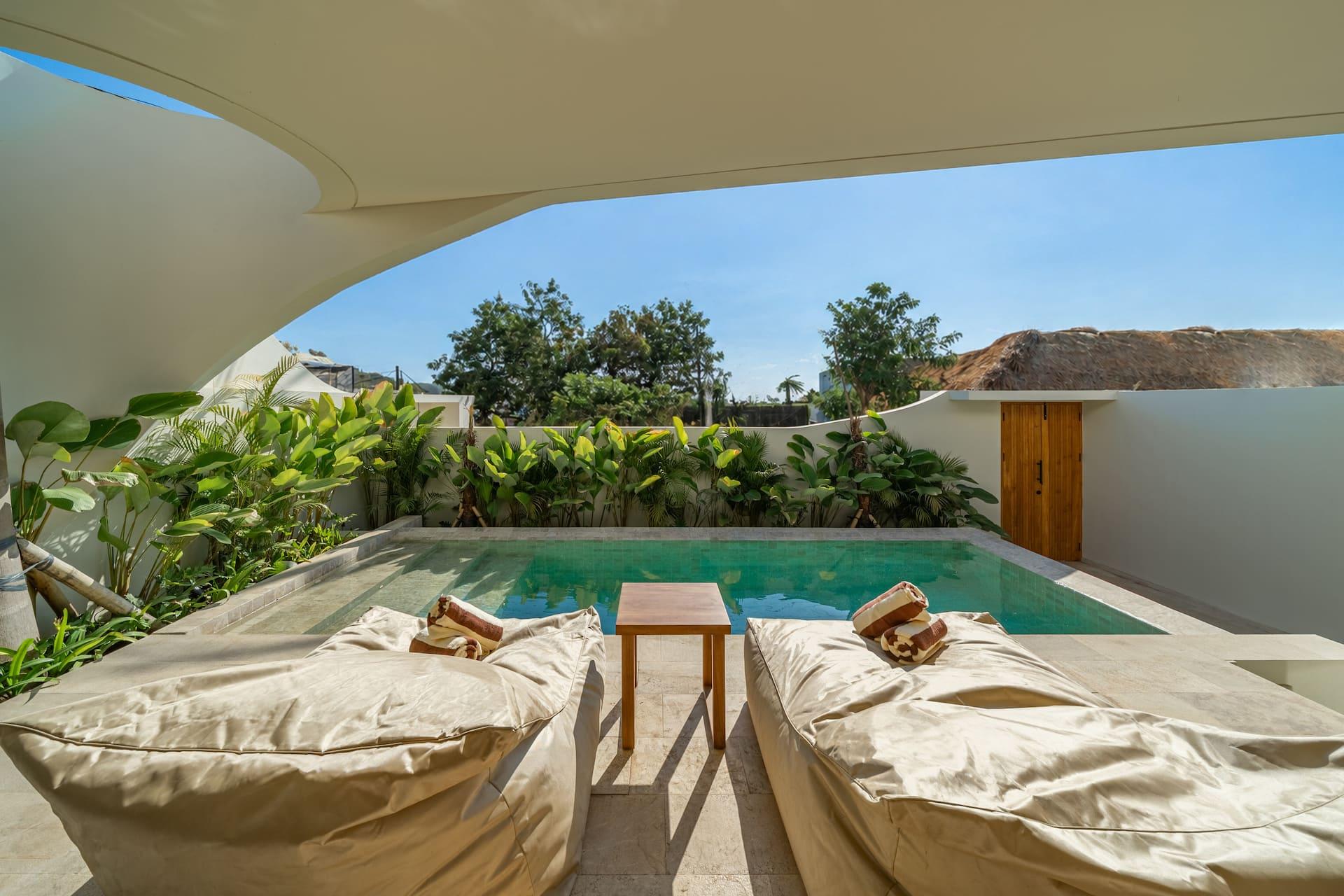 Oversized bean-bag loungers and a low teak table on the travertine pool deck at Villa Amber