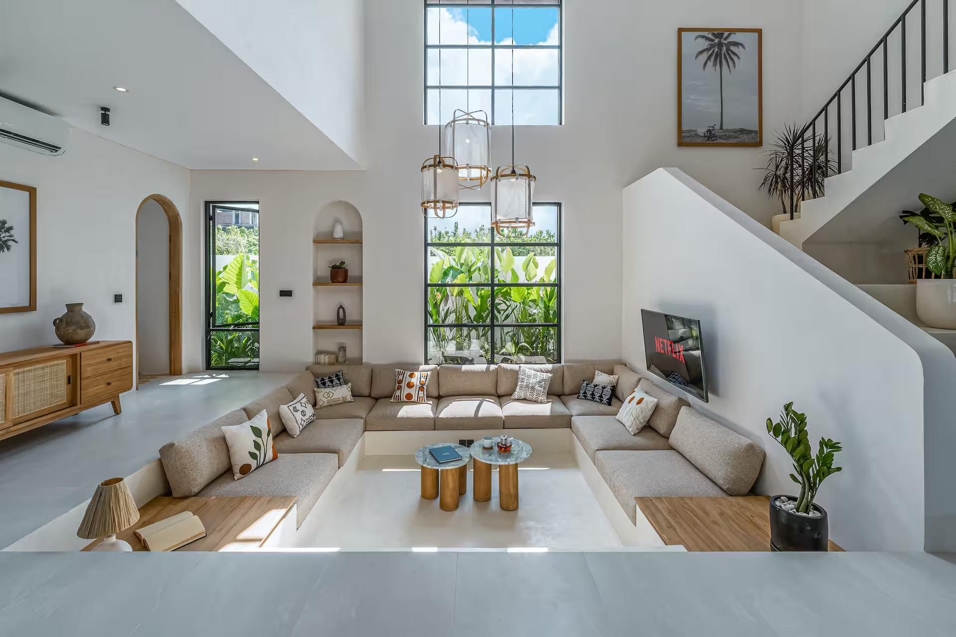 Double-height living room with a sunken banquette lounge and a white staircase behind