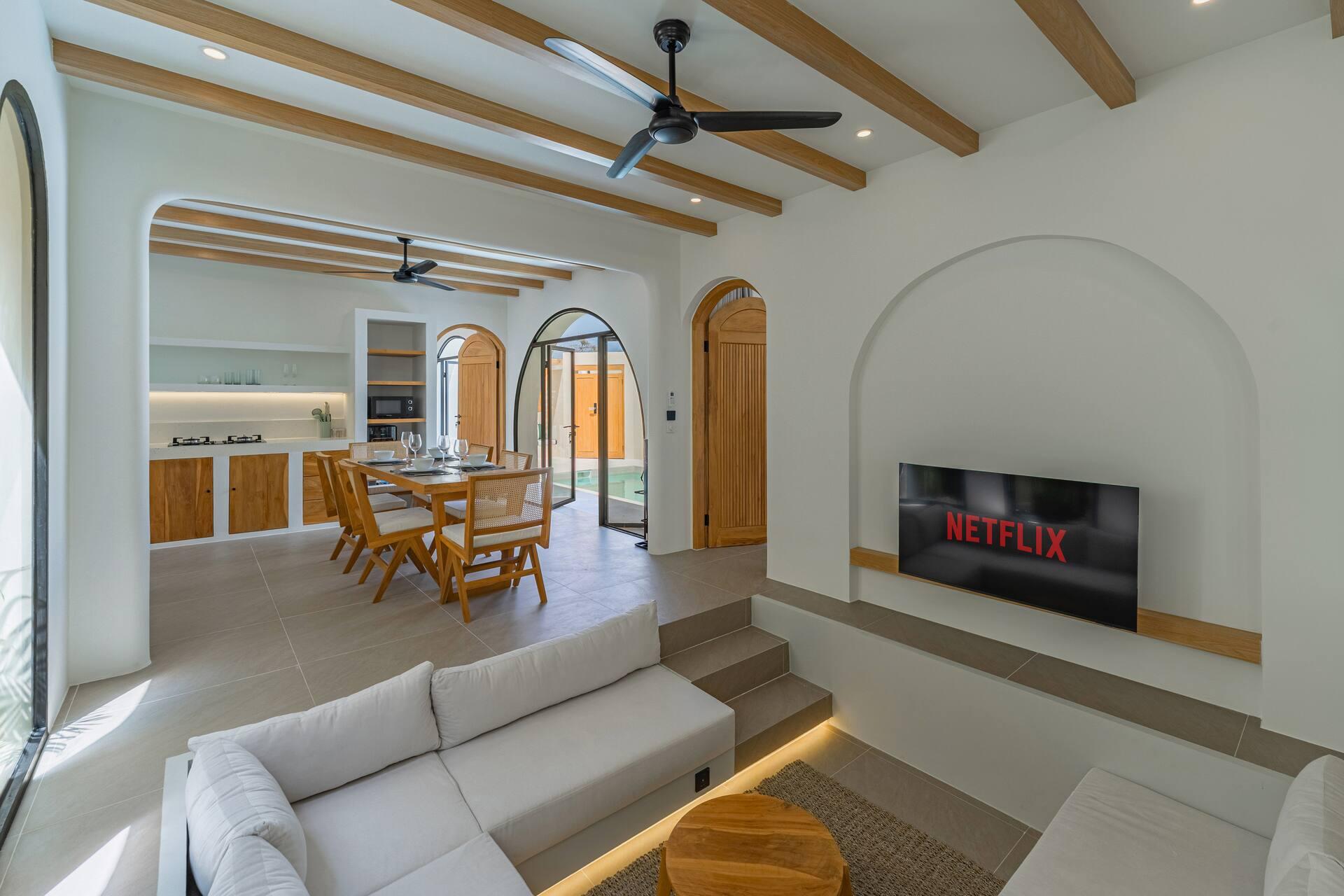 Sunken lounge with a white corner sofa, TV in an arched niche and timber-beamed ceiling at Villa Solmea