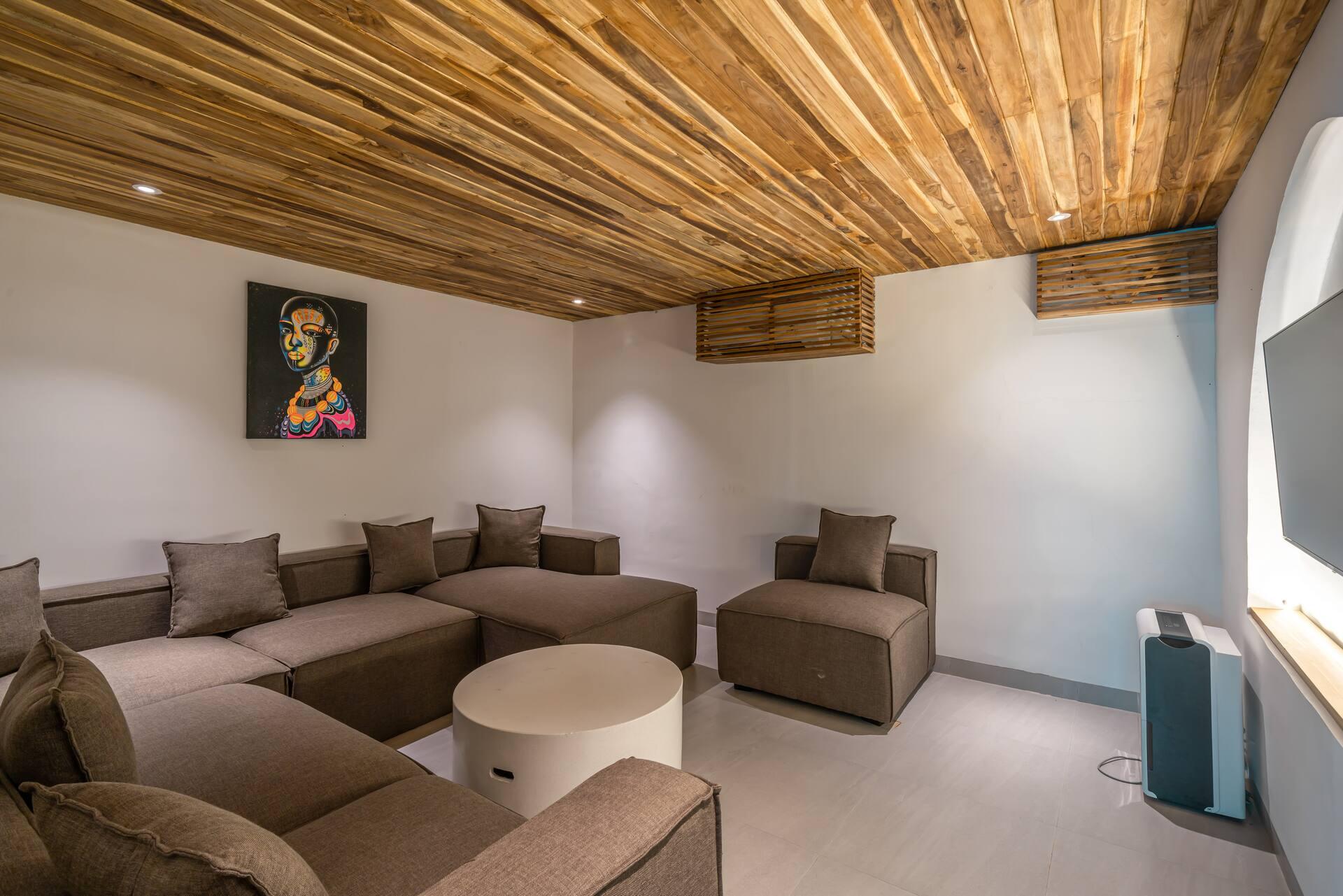 Lounge with deep brown modular sofas, round white coffee table and bold artwork under a slatted timber ceiling