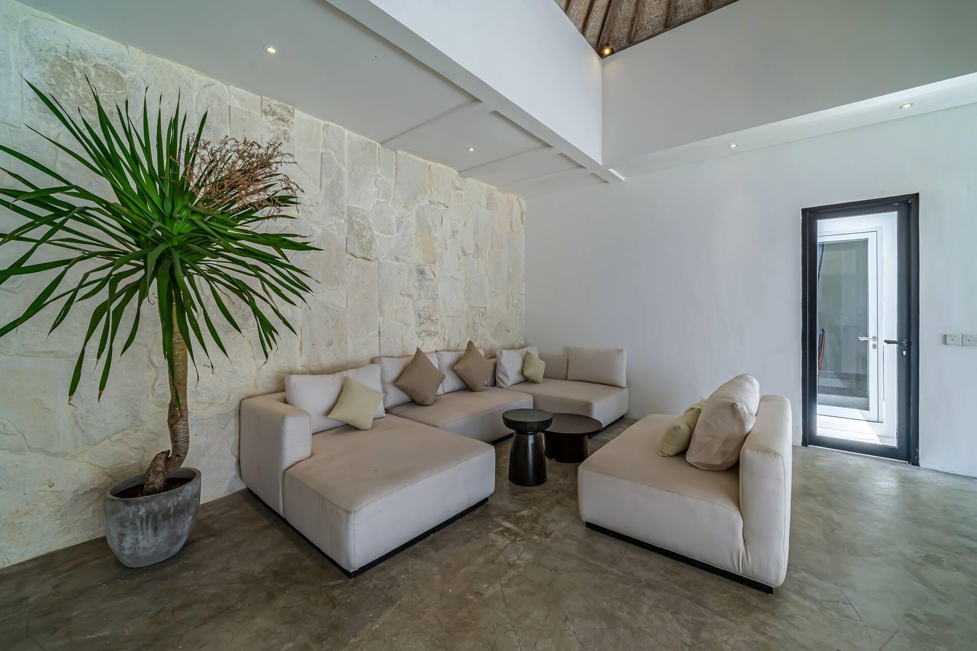 Living room with cream sofas and a potted palm against a pale textured stone wall at Villa Zenaya