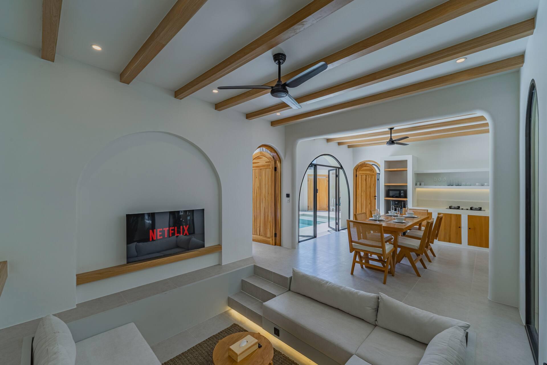 Sunken lounge with a pale corner sofa, TV in an arched niche and the dining room beyond at Santai Escape
