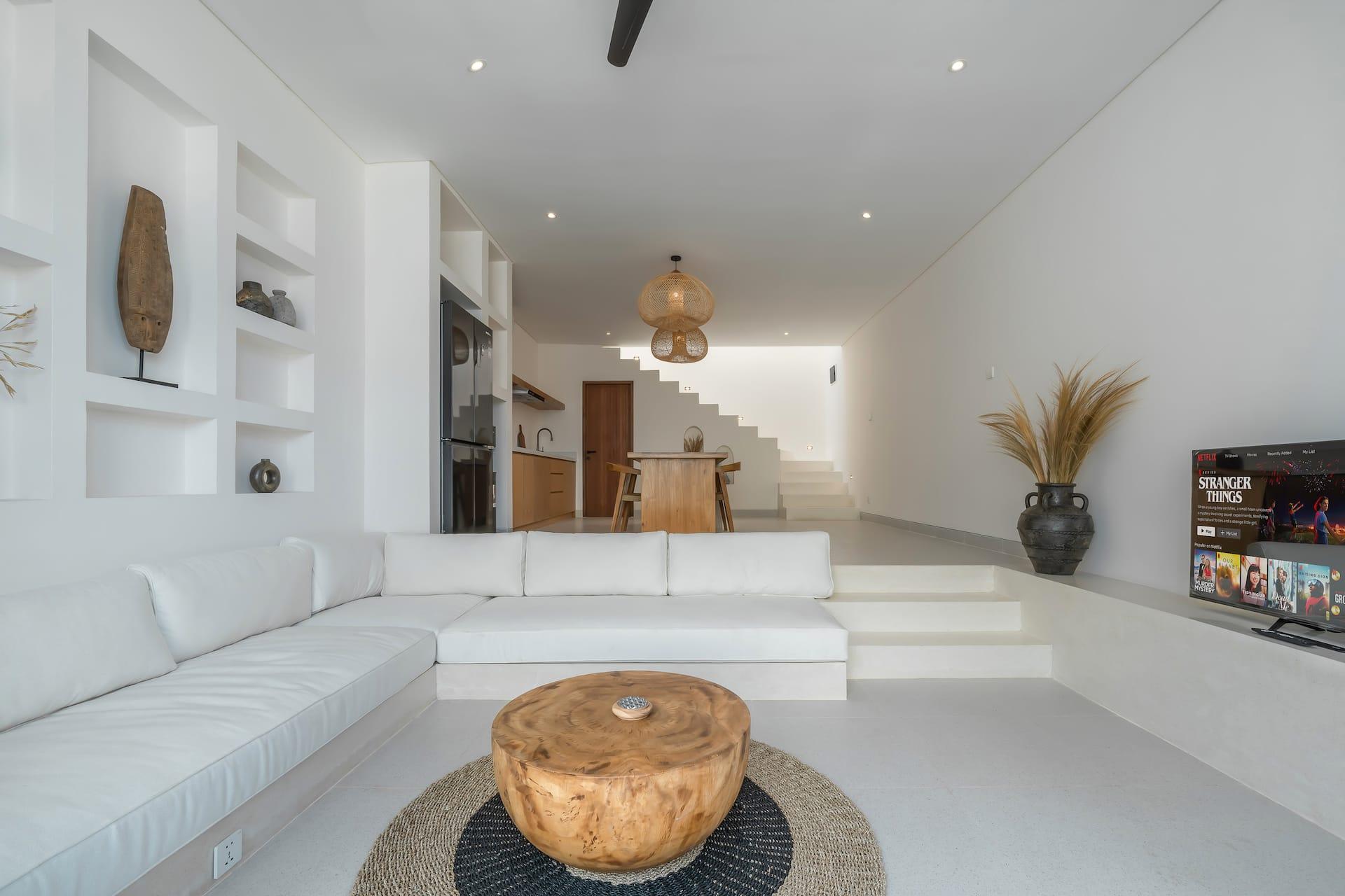 Sunken white lounge with a long built-in sofa and a carved timber coffee table on a round rug