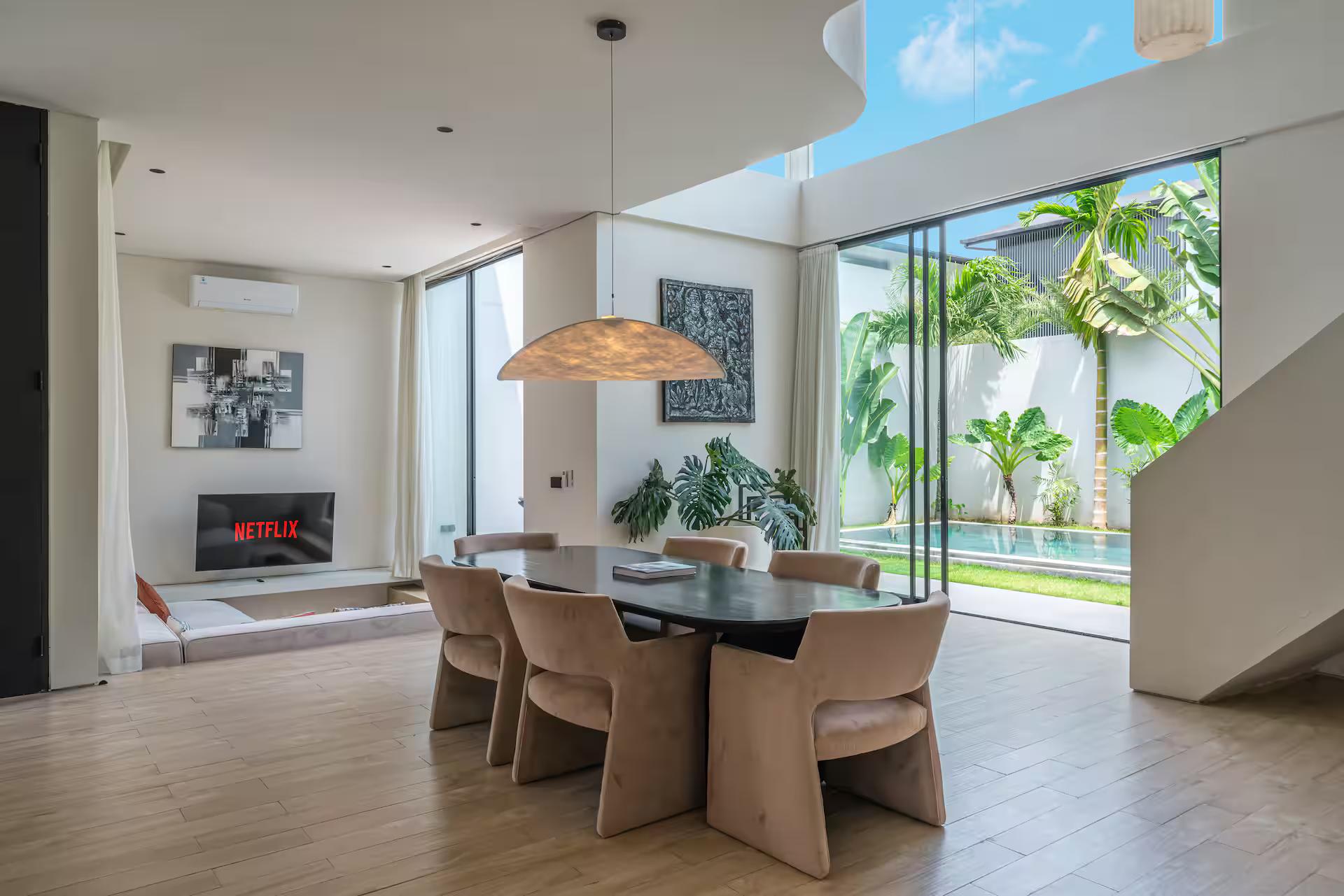 Dining table and fluted chairs beside the linear fireplace, glass wall open to the pool