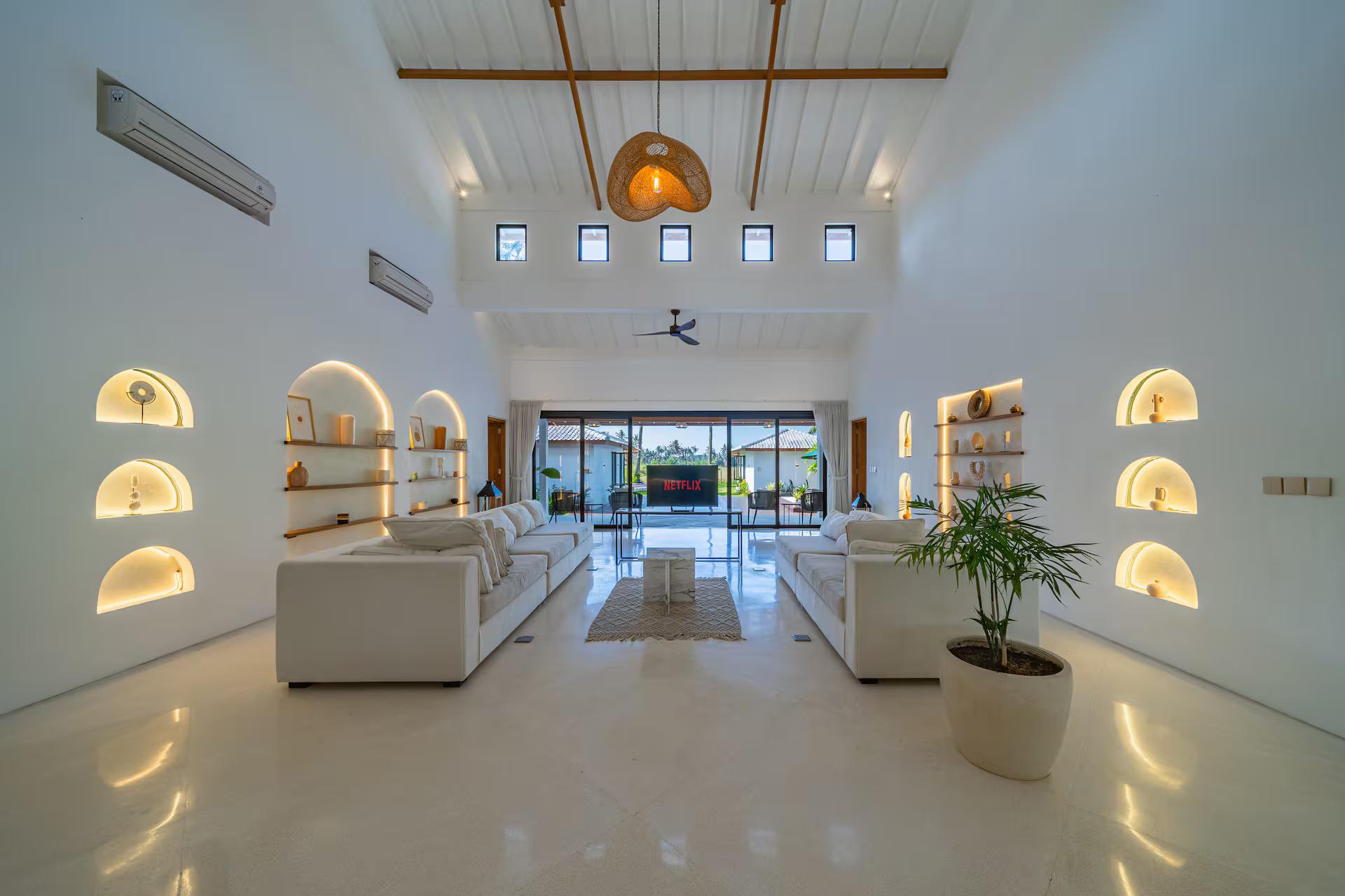 Open living room under a white shiplap ceiling, arched niches lit from within behind the sofas
