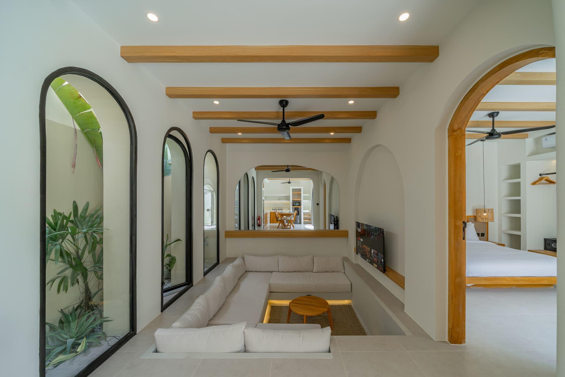 Sunken lounge with a built-in white sofa, round timber table and arched black-framed windows