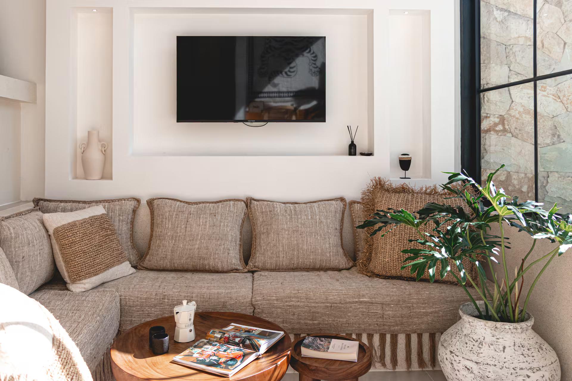 The plaster banquette in oatmeal linen with a round timber table and a television in an arched niche