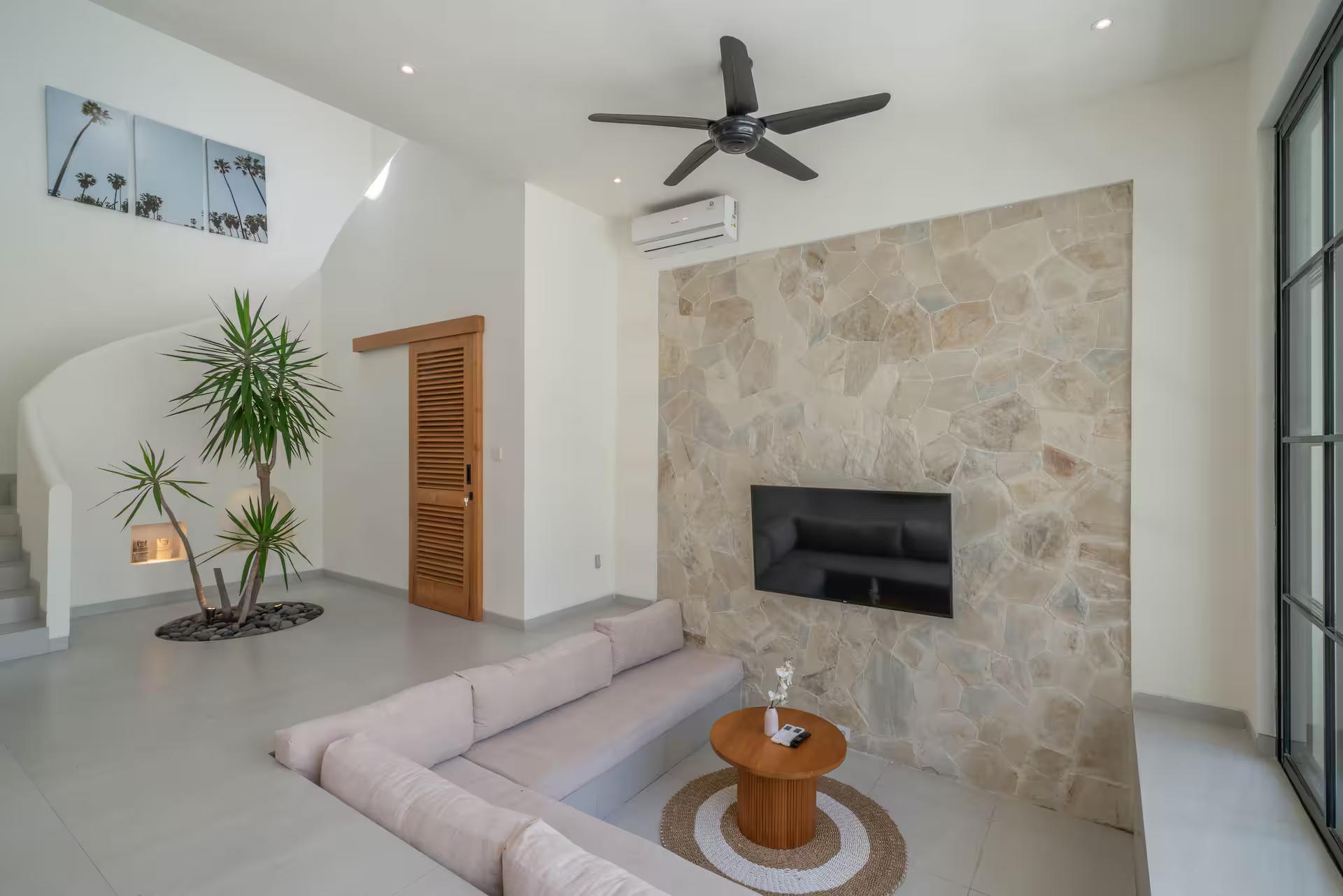 Sunken lounge at Villa Yuri, television on a rough stone wall and a palm growing indoors