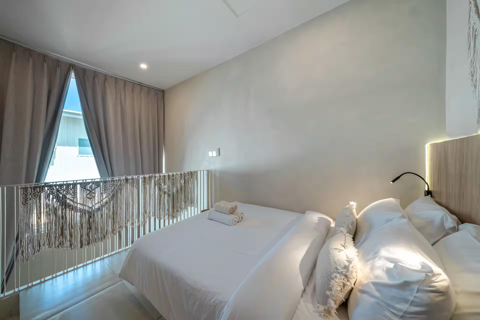 The mezzanine bedroom, king bed behind a macrame-hung steel rail and a gable window