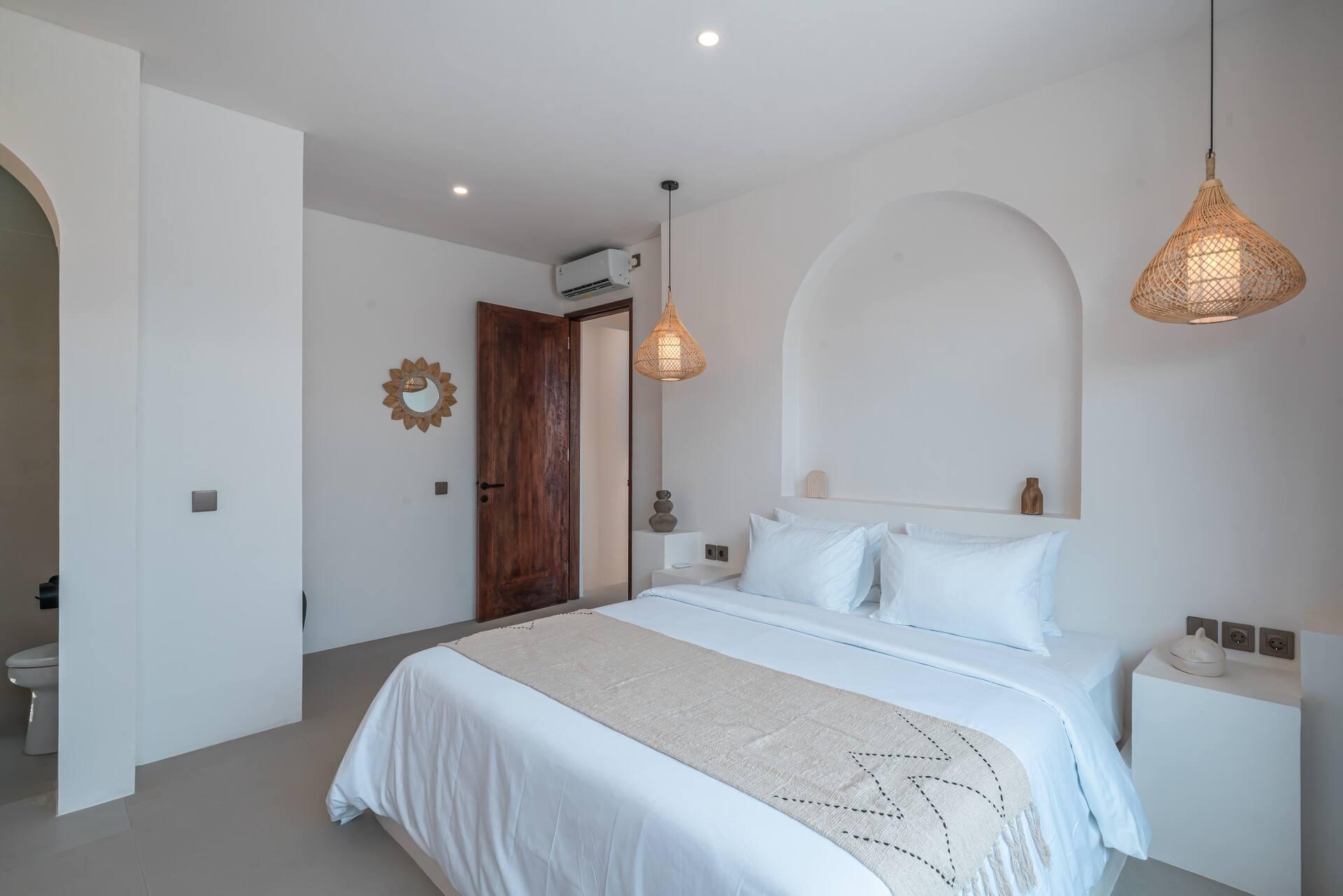 King bed set into its own plaster arch at Nova Oasis 3, rattan pendant hanging alongside