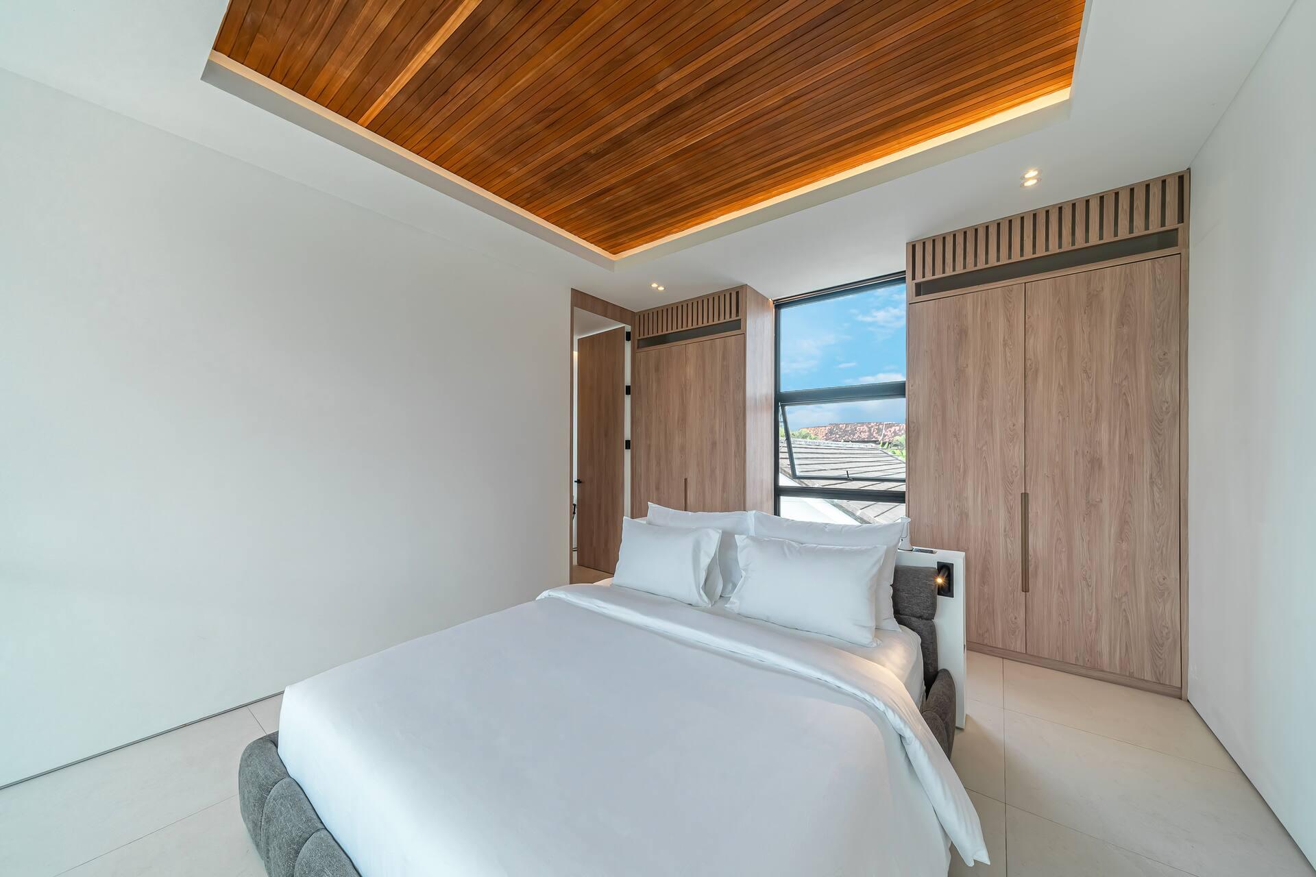 King bedroom under a timber-slatted ceiling, with garden windows and warm natural tones