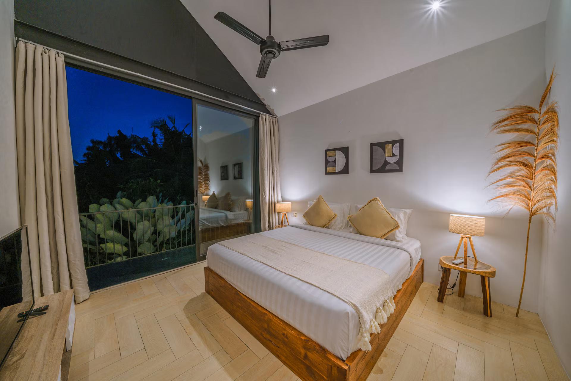Bedroom with a timber-framed bed under a vaulted ceiling, glass doors open to the garden