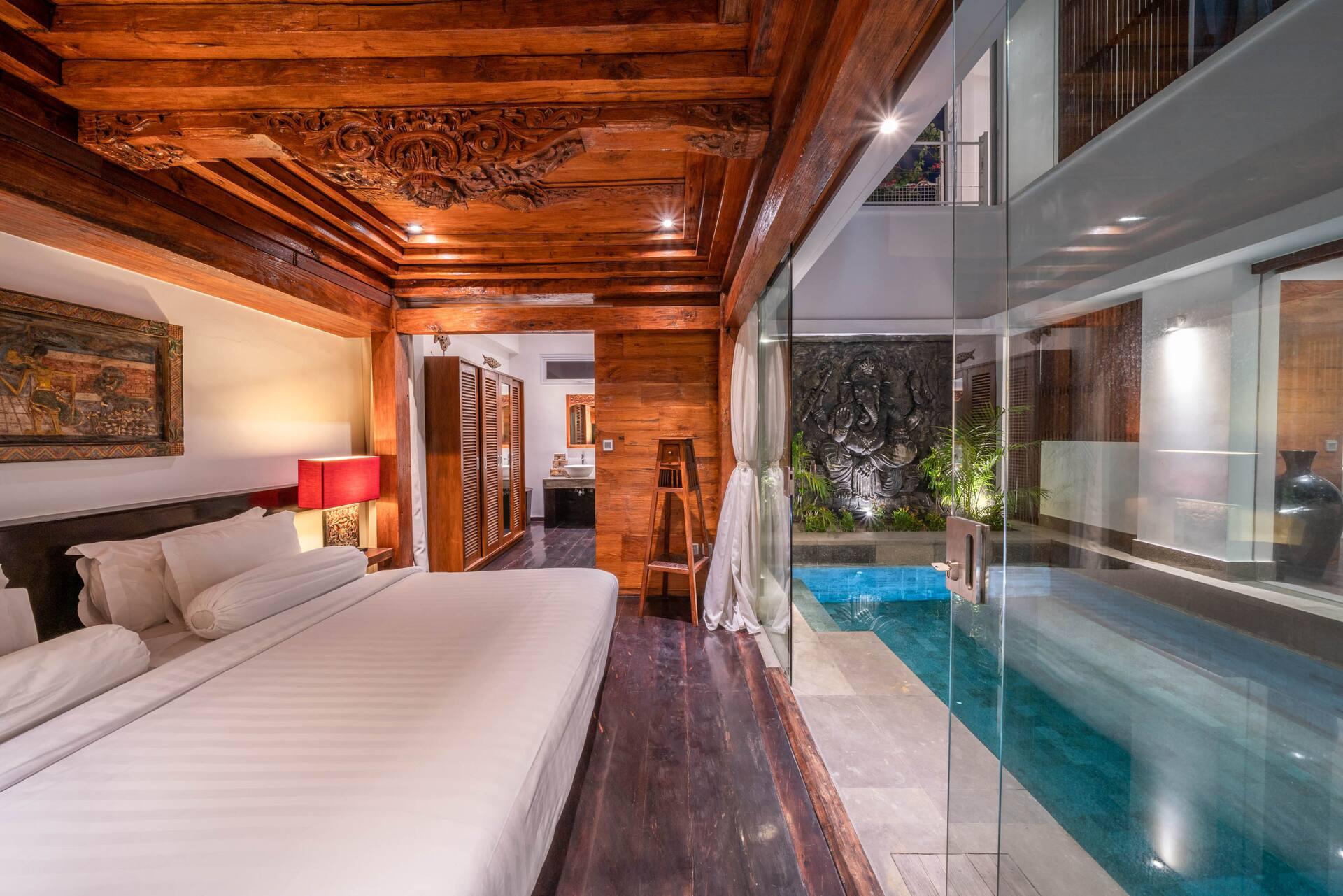 Ground-floor bedroom at Villa Tykhe beneath a carved timber ceiling, opening to the pool