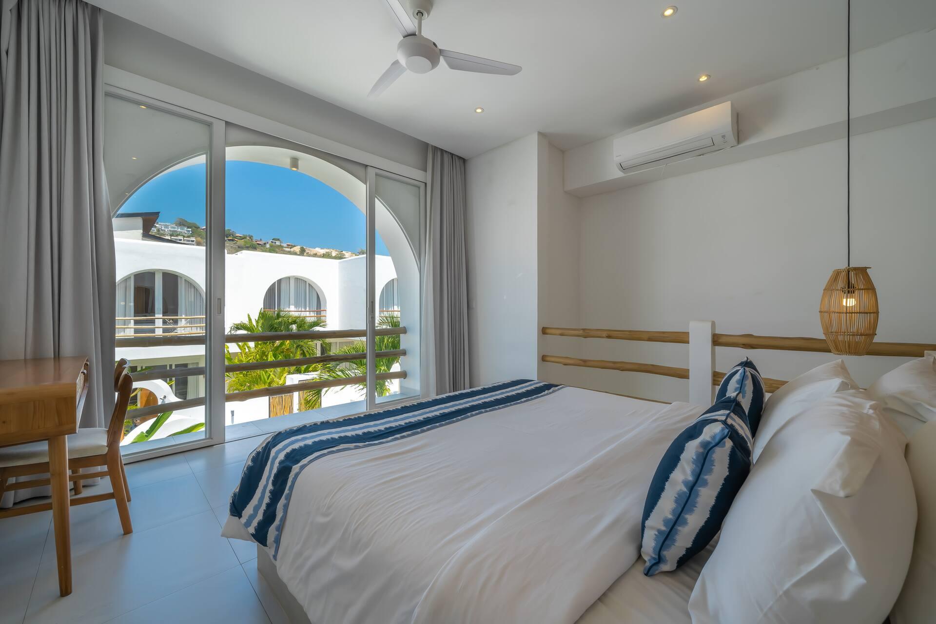 King bedroom with a timber-slat headboard and indigo linen, opening onto its own arched balcony