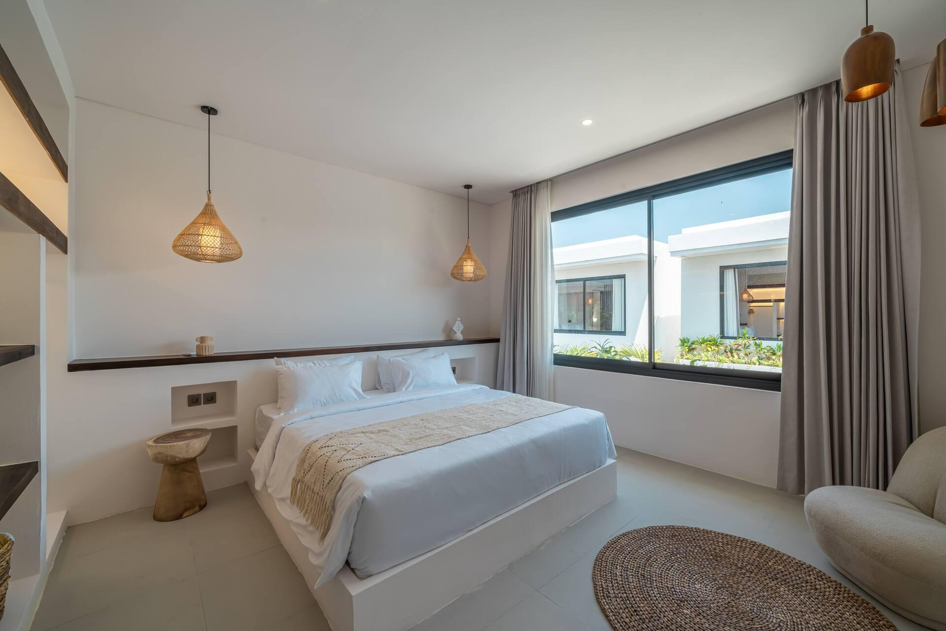 Upstairs bedroom with a king bed, paired rattan pendants and a wide window over the rooftops