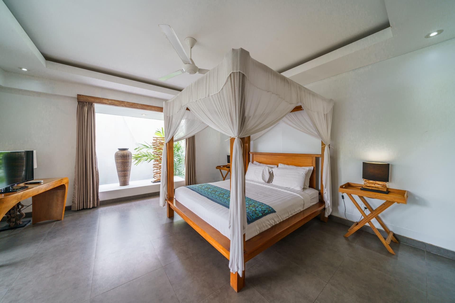 Upstairs bedroom with a carved teak four-poster hung in white drapes and a timber desk