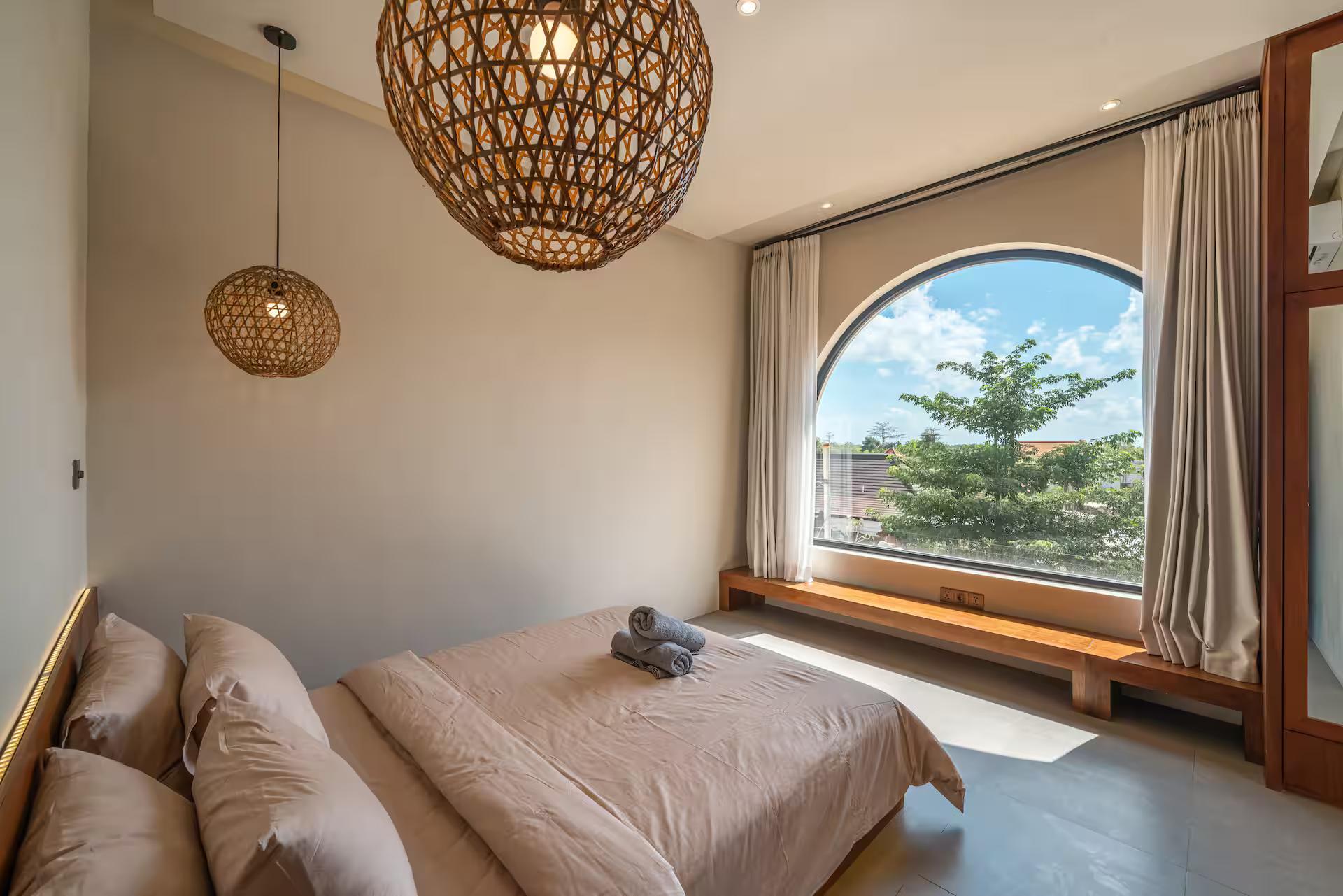 Bedroom with a half-round arched window and a long timber bench beneath it, framing a tree