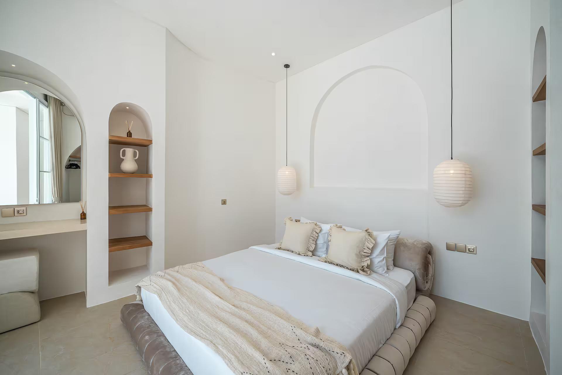 King bed on a fluted plaster base set into an arched recess, paper pendants either side