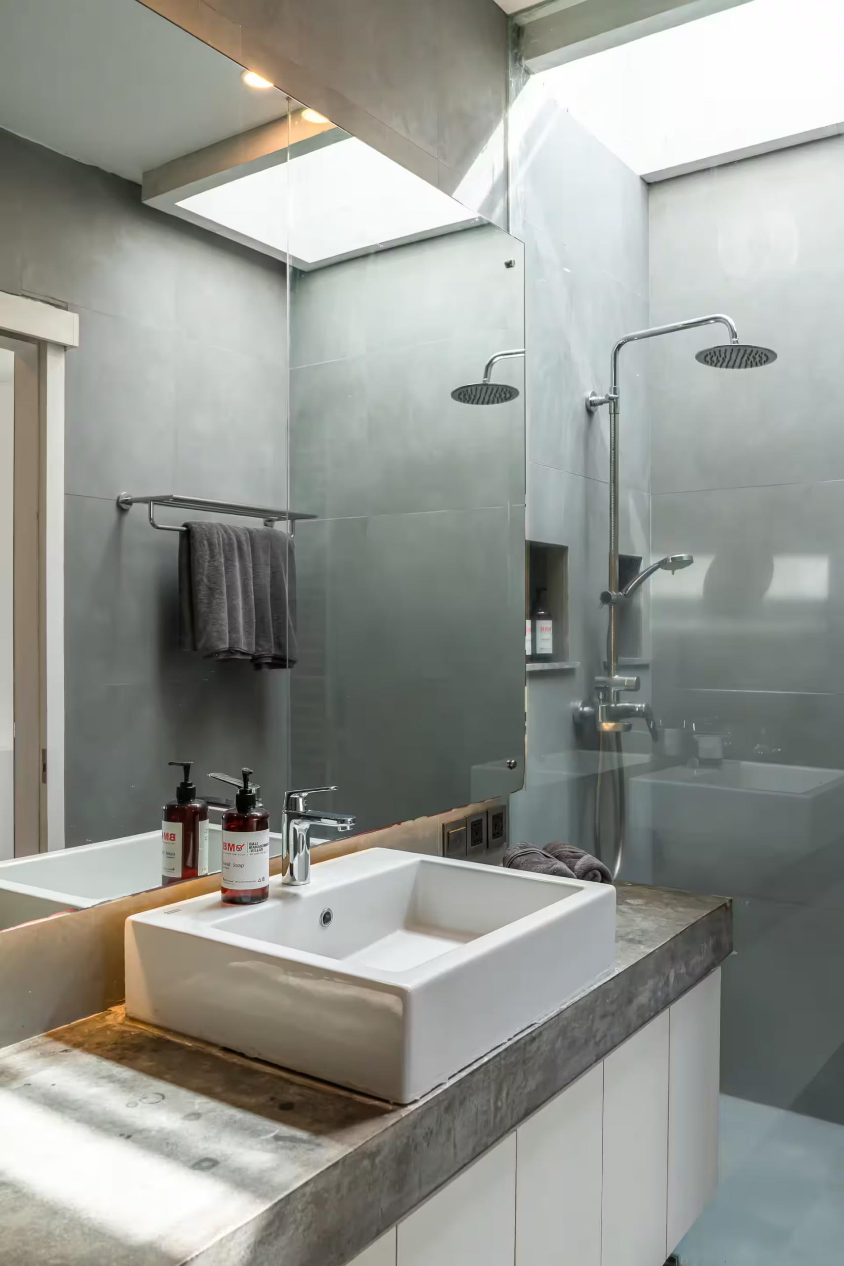 En-suite lined in raw concrete with twin rain showers and a stone vessel basin