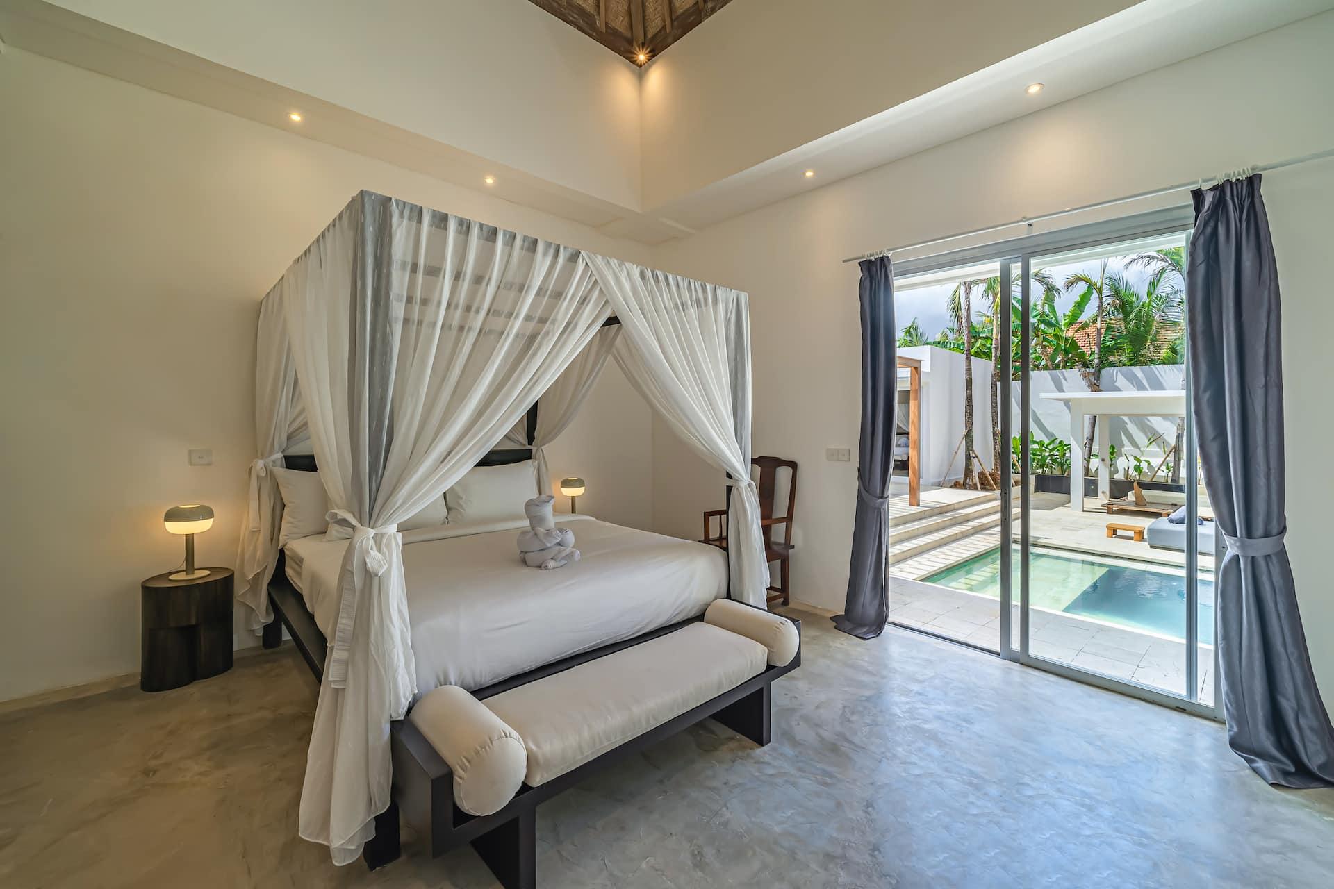 Four-poster canopy bed draped in white voile, with sliding glass doors opening to the pool