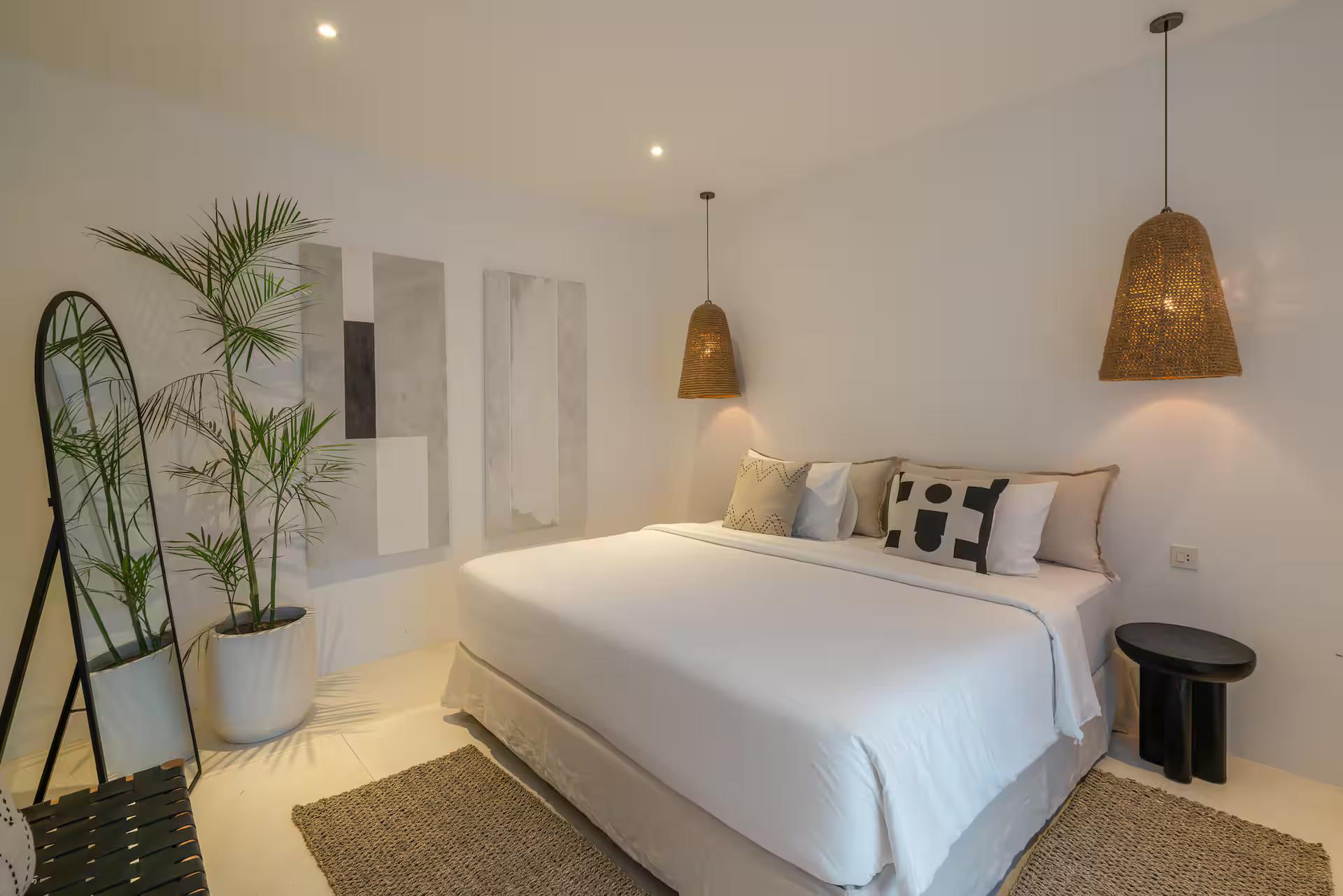 King bedroom with a tall arched mirror, a potted palm and twin rattan pendant lights