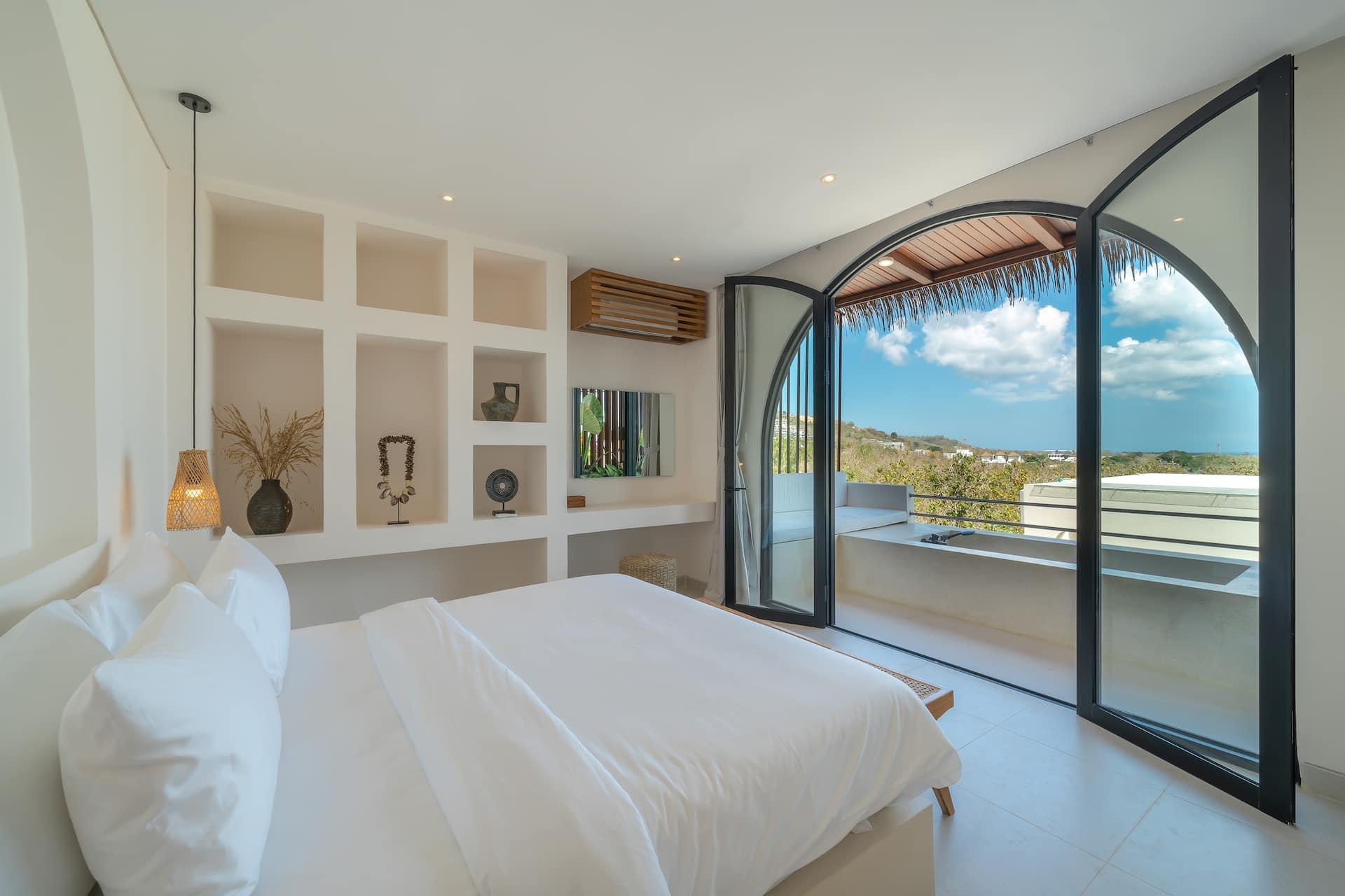 Villa Adiwarna bedroom with arched glass doors open to the balcony and a view to the sea