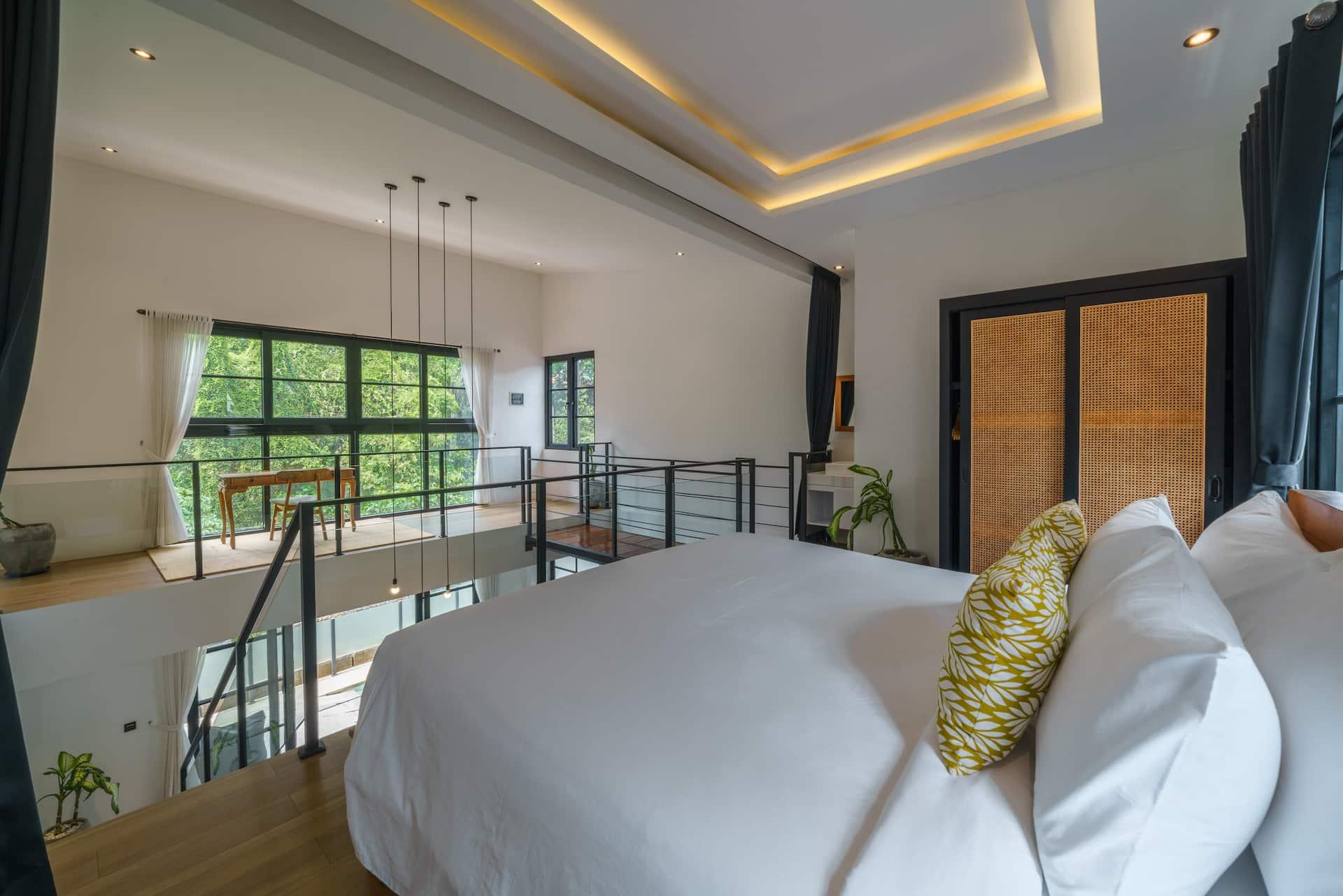 Mezzanine bedroom with a king bed, cove lighting and black-framed windows onto greenery