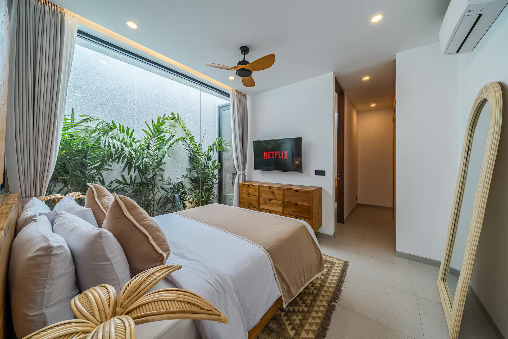 King bedroom at Uluwatu Tropical Estate with banked cushions, a wall-mounted television and an arched mirror