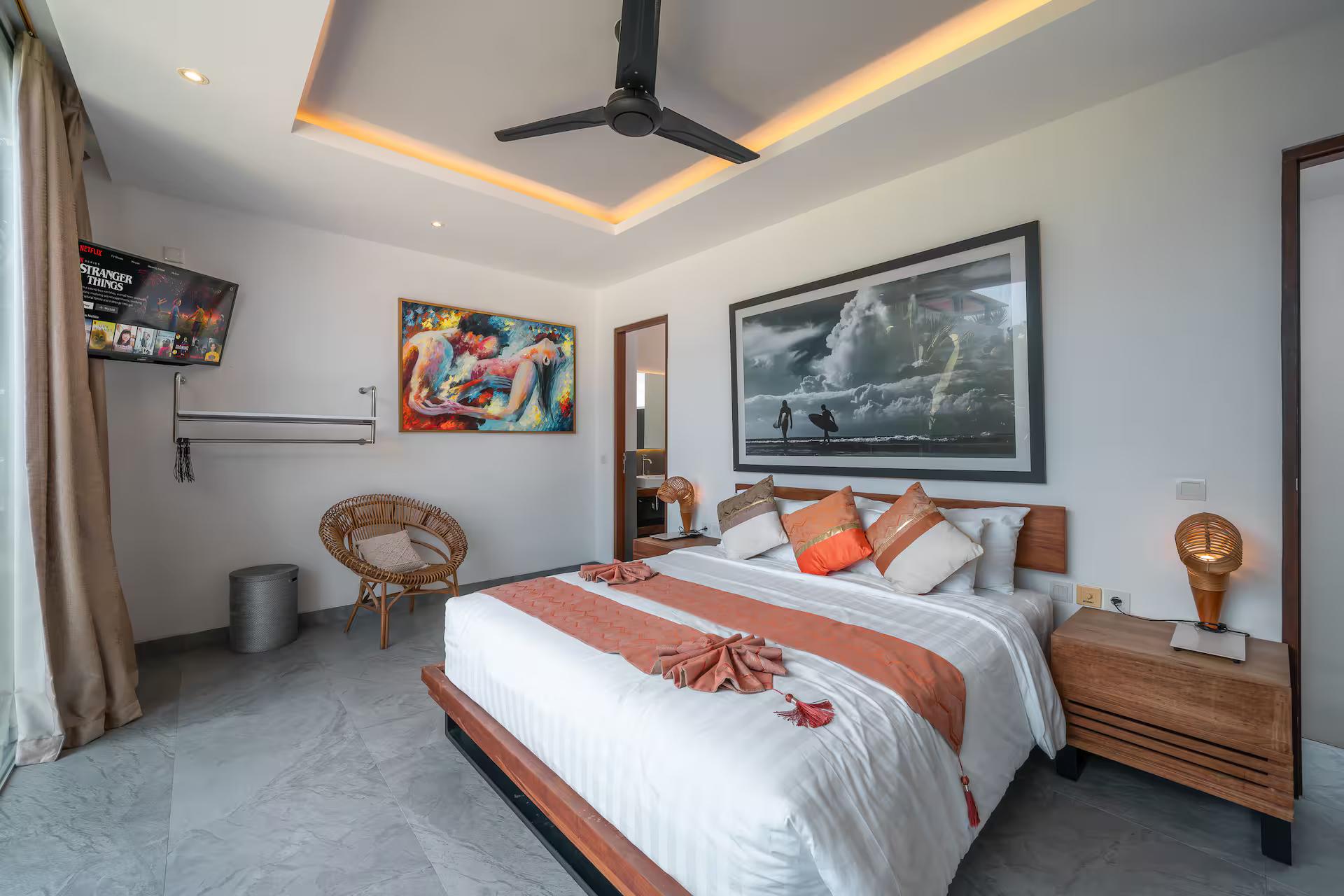 King bedroom at The Jendela House with a surf photograph, rattan chair and garden glazing
