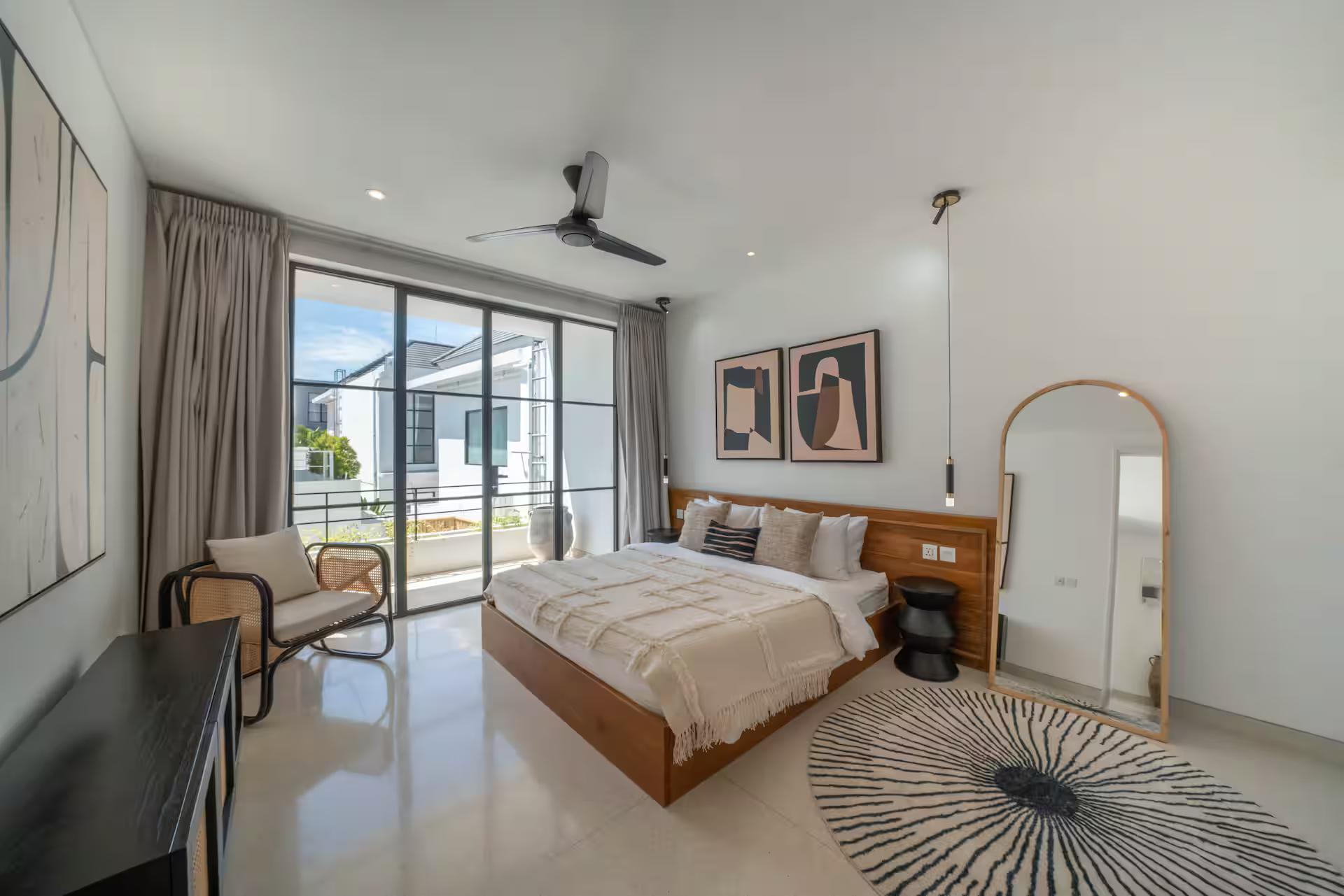 A king bedroom with a teak platform bed, black console and a tall arched floor mirror
