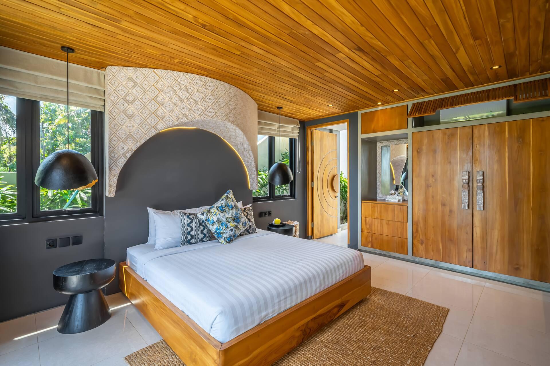 King bedroom at Villa Asri Nyanyi, a curved plaster arch behind the bedhead and black dome pendants