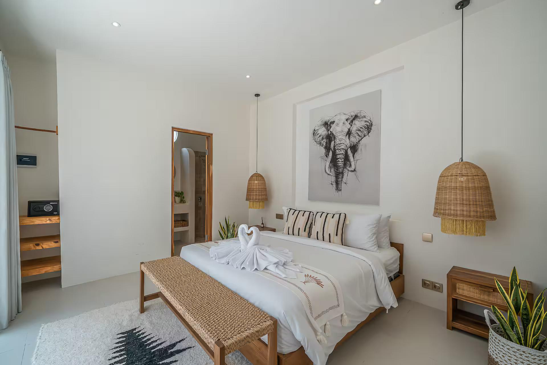 Queen bed beneath the hand-drawn elephant that gives Villa Gajah its name, rattan pendants either side