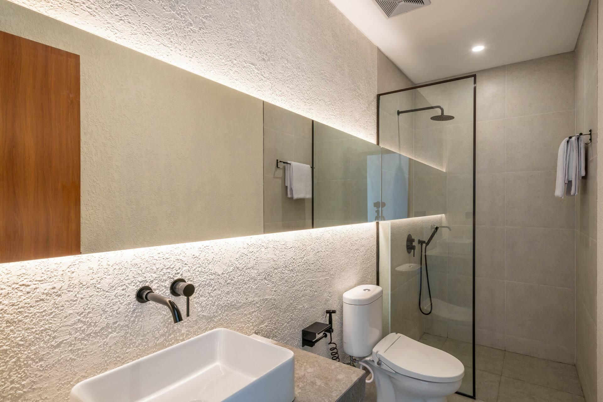 Bathroom with a textured lime-plaster wall, backlit mirror niche and a glass walk-in shower