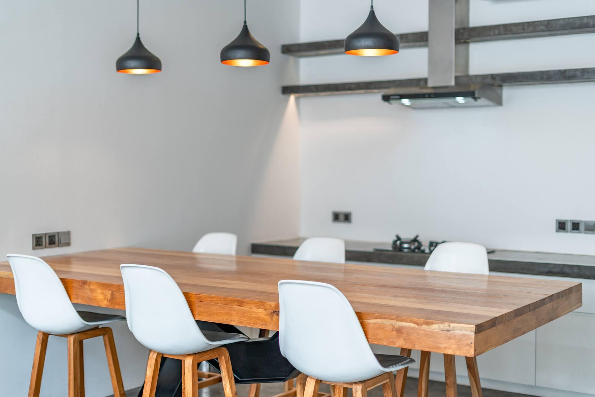 Long solid-timber table with moulded white chairs beneath black dome pendants